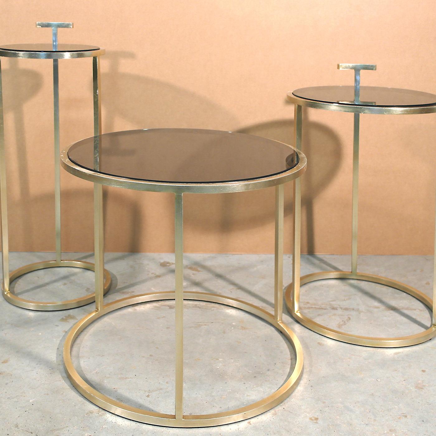 This round side table makes a sleek addition to the living room, boasting a circular brass base with a light brushed bronze finish. Characterized by pure lines and a geometric shapes, the design is finished with a bronze glass top. Exuding a modern