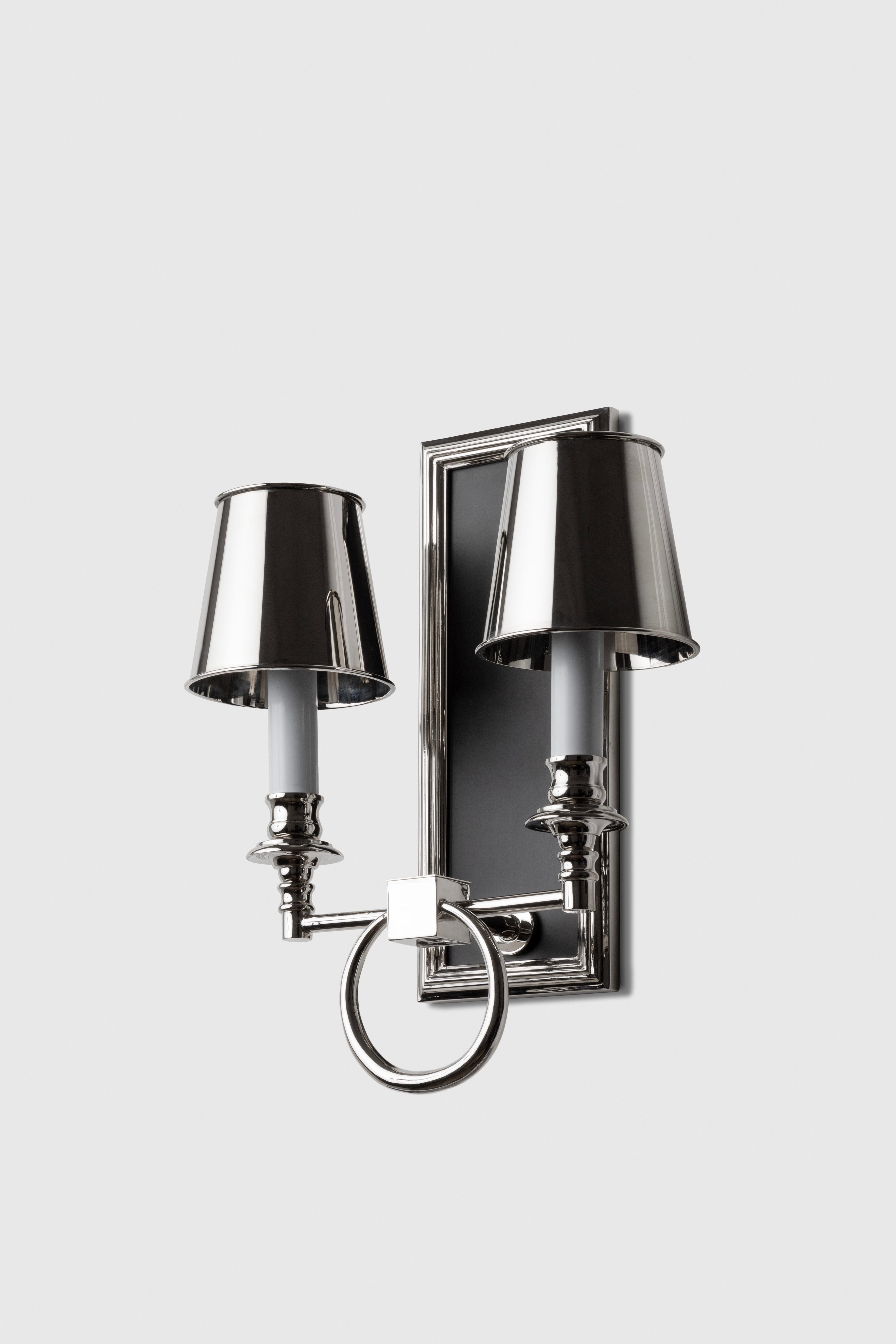 This sconce is made in bronze, with two lights and lampshades in a rectangular frame and with a ring detail in between the lights. 

This piece was designed by Fernanda Loyzaga at the end of 2023. We always abide by the harmonic proportions. The