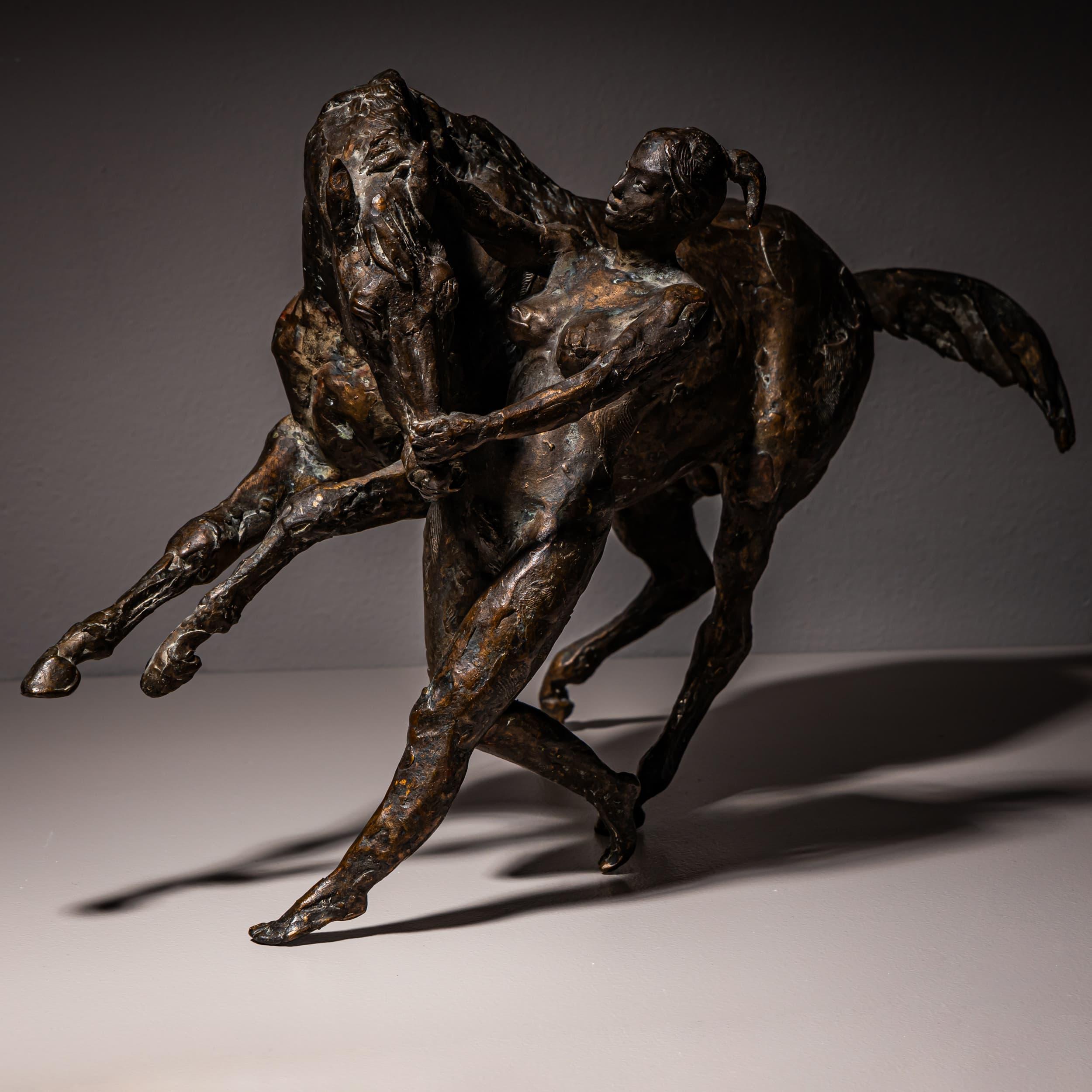 Large bronze sculpture depicting a dynamic scene of a rearing horse being tamed by a female nude. The surface treatment shows strong, expressive modeling that emphasizes the energy of the composition. An illegible incised signature is present on the