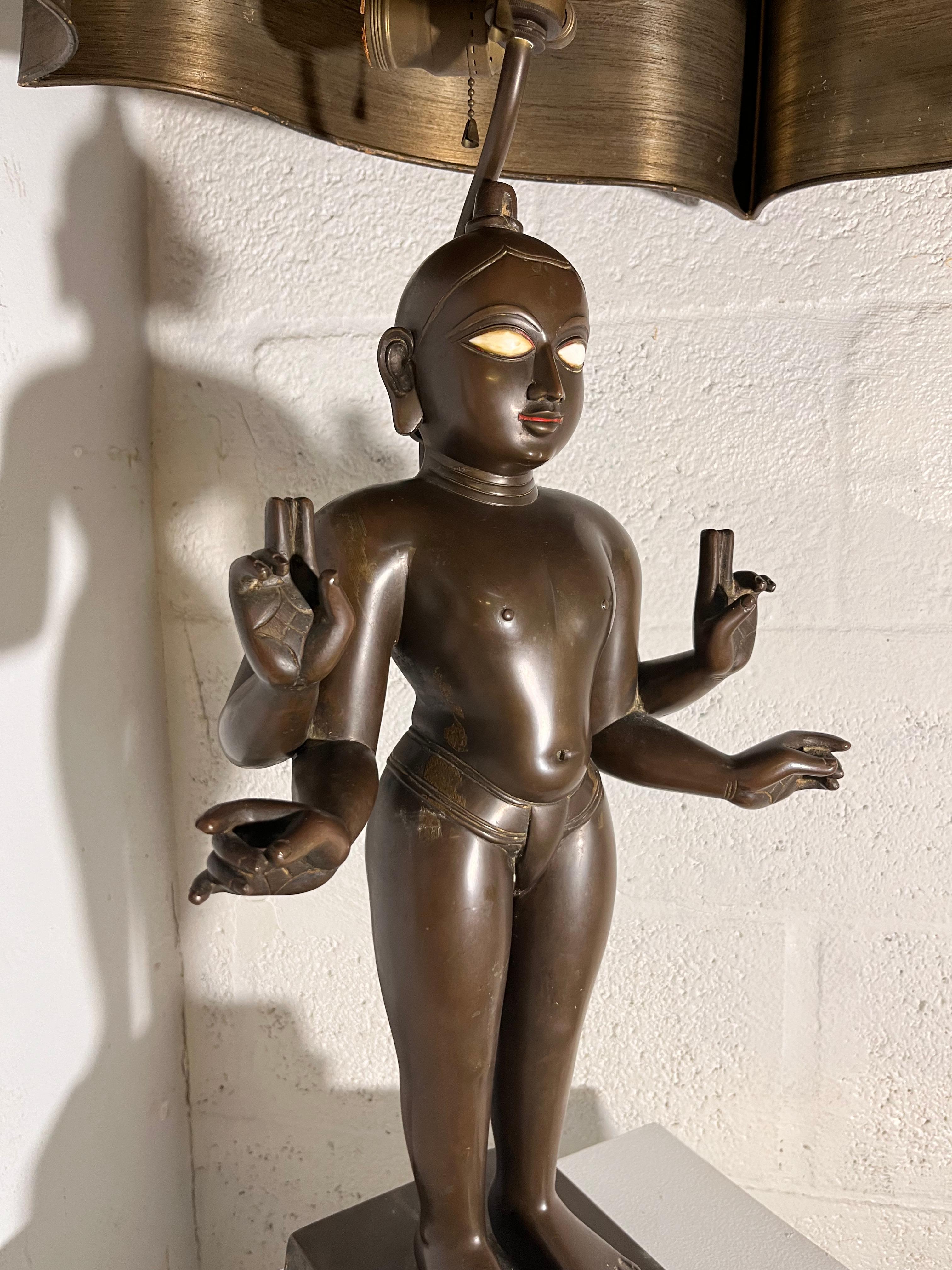 Statue-lampe représentant le dieu hindou Vishnu. La statue semble dater de la fin du XIXe siècle ou du début du XXe siècle. Il est en bronze ordinaire. Il est placé sur un piédestal. La lampe est vendue avec un abat-jour en métal cuivré qui donne un