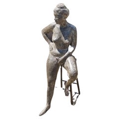 Bronze sculpture of a seated female nude on a stool.