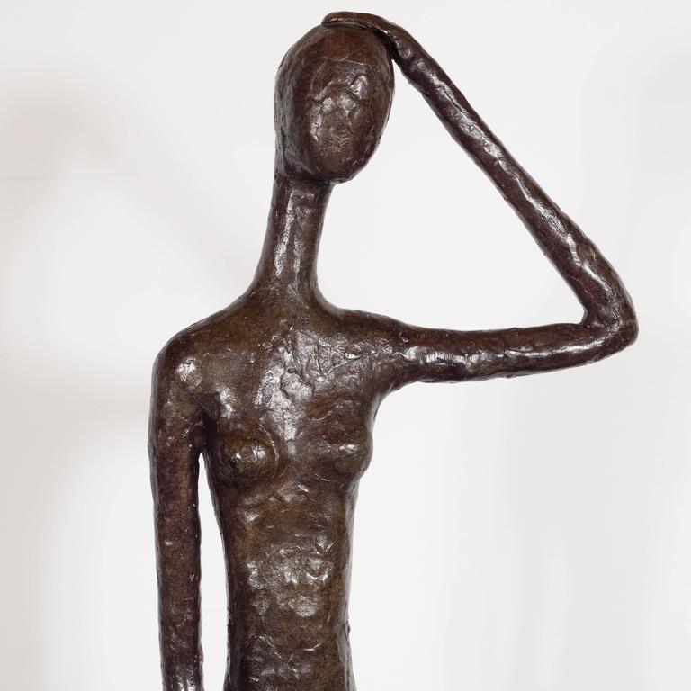 A bronze sculpture of a standing nude in the style of Giacometti, by L. Salzmann, signed by the artist, representing a standing woman with one arm raised to her head mounted on a square bronze base, an attractive sculpture in the style of Giacometti