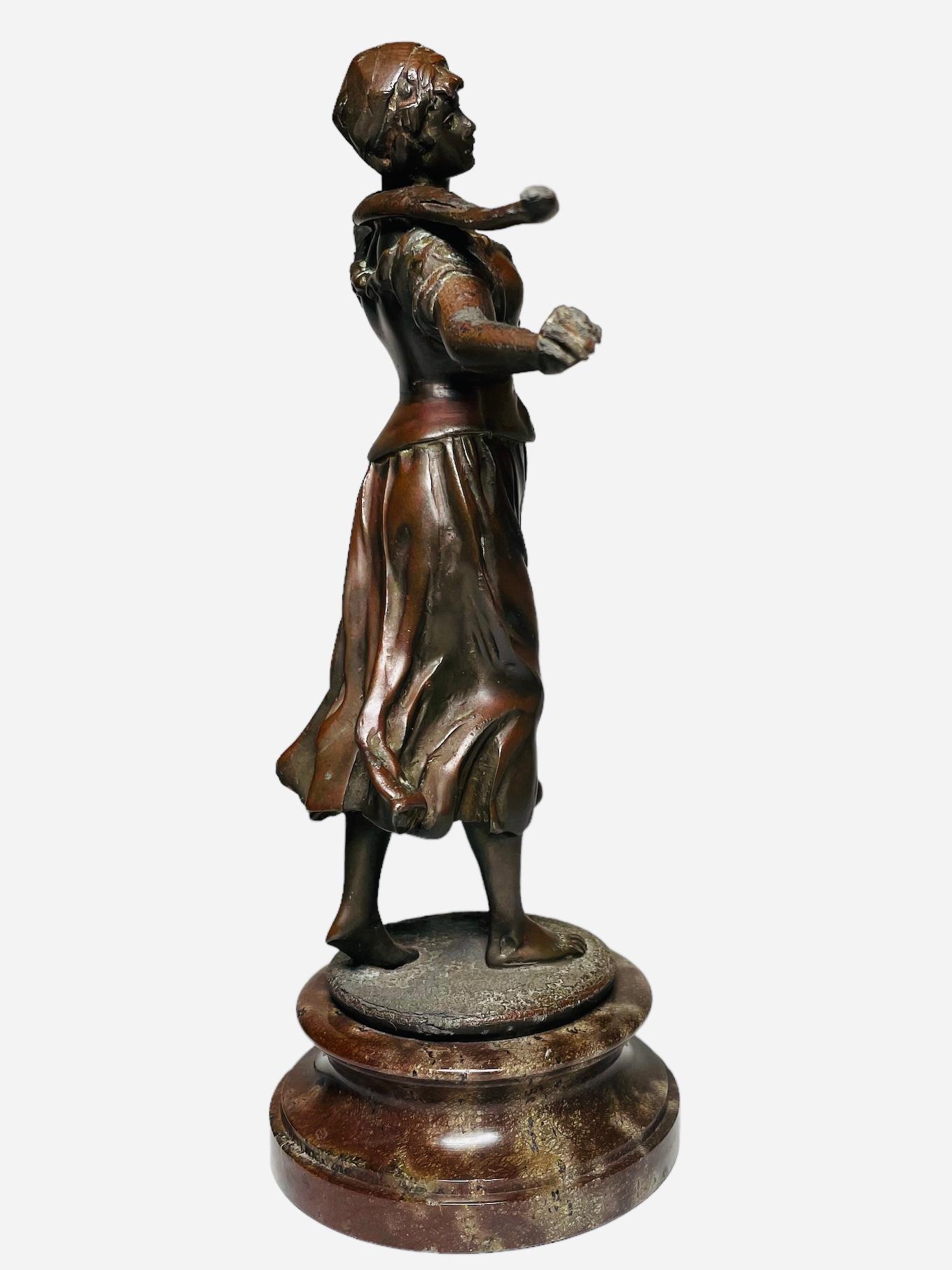 This is a bronze Sculpture of a Woman Water Bearer. It depicts a patinated bronze sculpture of a barefoot young woman peasant carrying a wood stick at the back of her neck. The sculpture is standing over a round wide marble base.