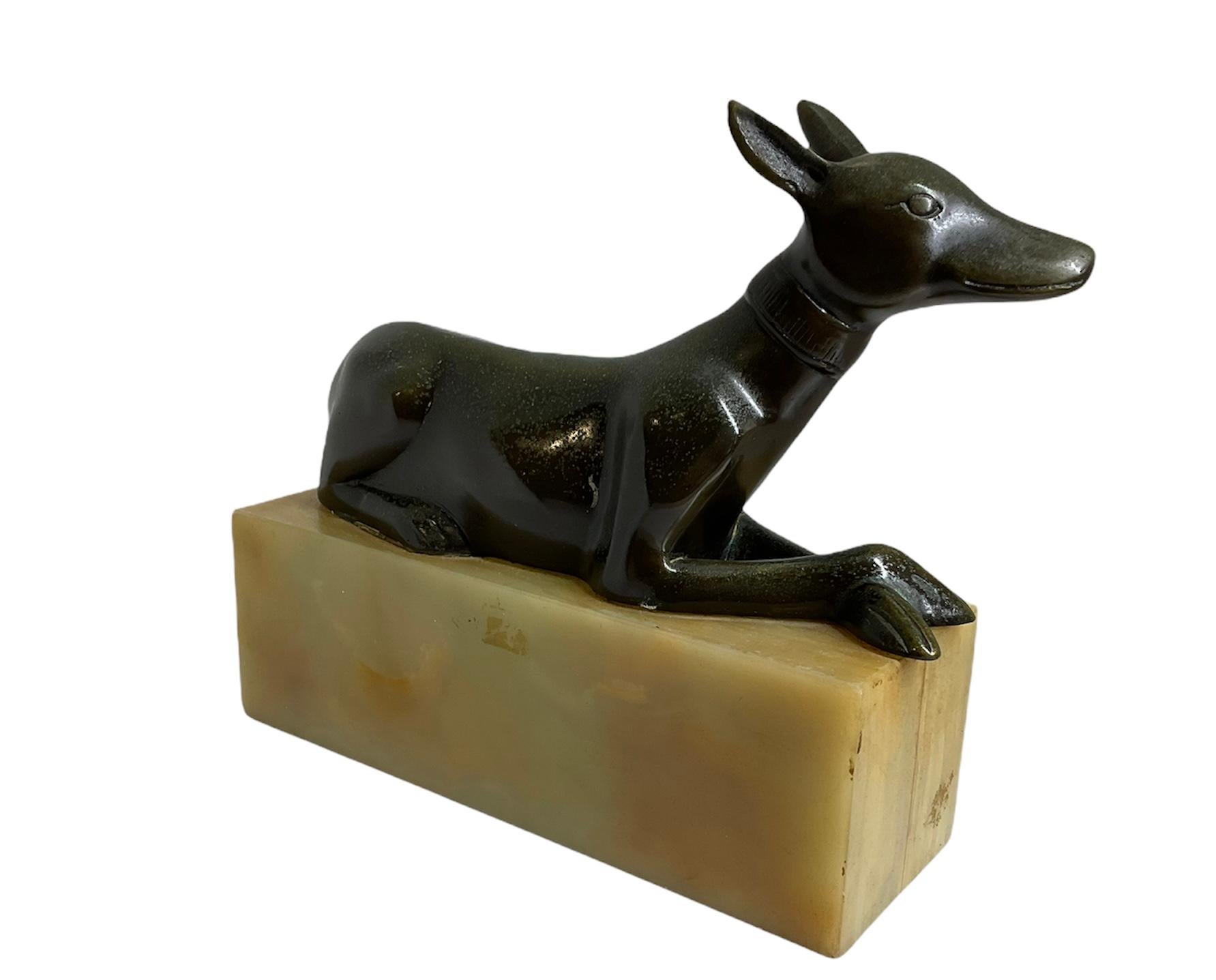 This is a patinated bronze sculpture of an Egyptian dog/Anubis laying down and supported by a rectangular green orange marble base. It is adorned by a neck collar.