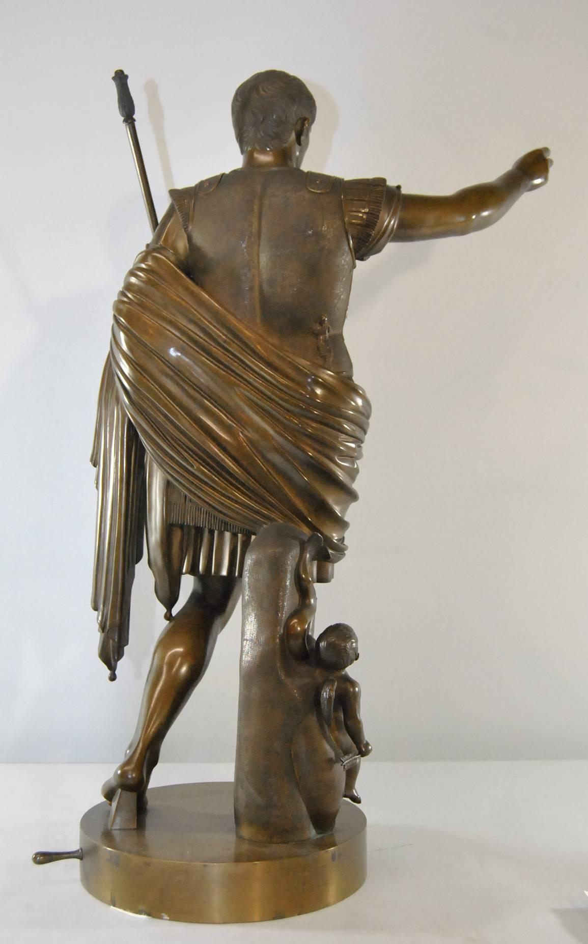 A finely cast patinated bronze of Augustus of Prima Porta: Modeled as a standing Caesar holding a scepter, having a putto at his feet astride a dolphin, with raised decoration on his chest plate; medium brown patina. Statue is 25.75