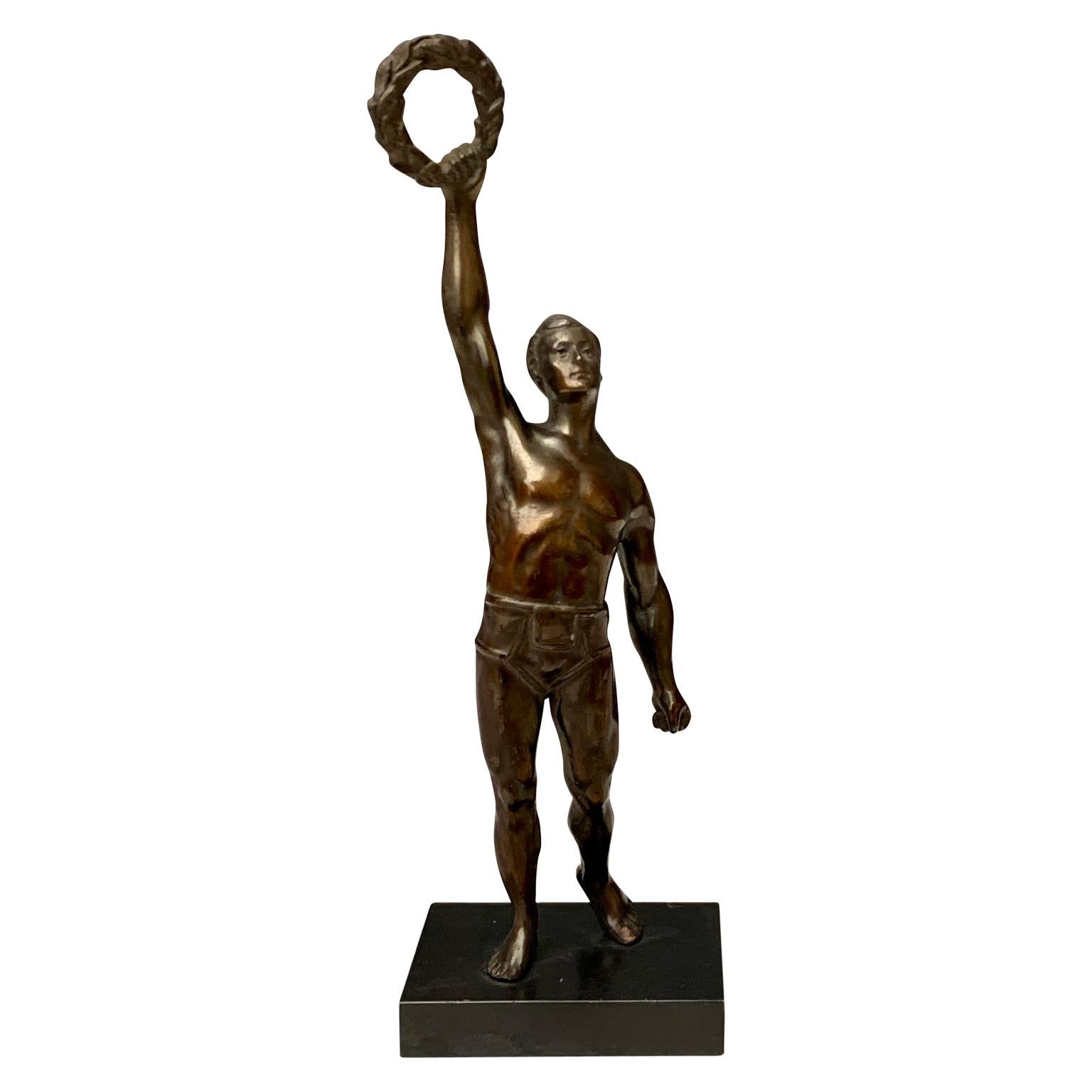 An Art Deco period sculpture in bronze on a metal base of an Olympic man who has just won. He holds the laurel-crown in with his right hand lifted up in sign of victory. This early 20th Century decorative object could have been made as a trophy for