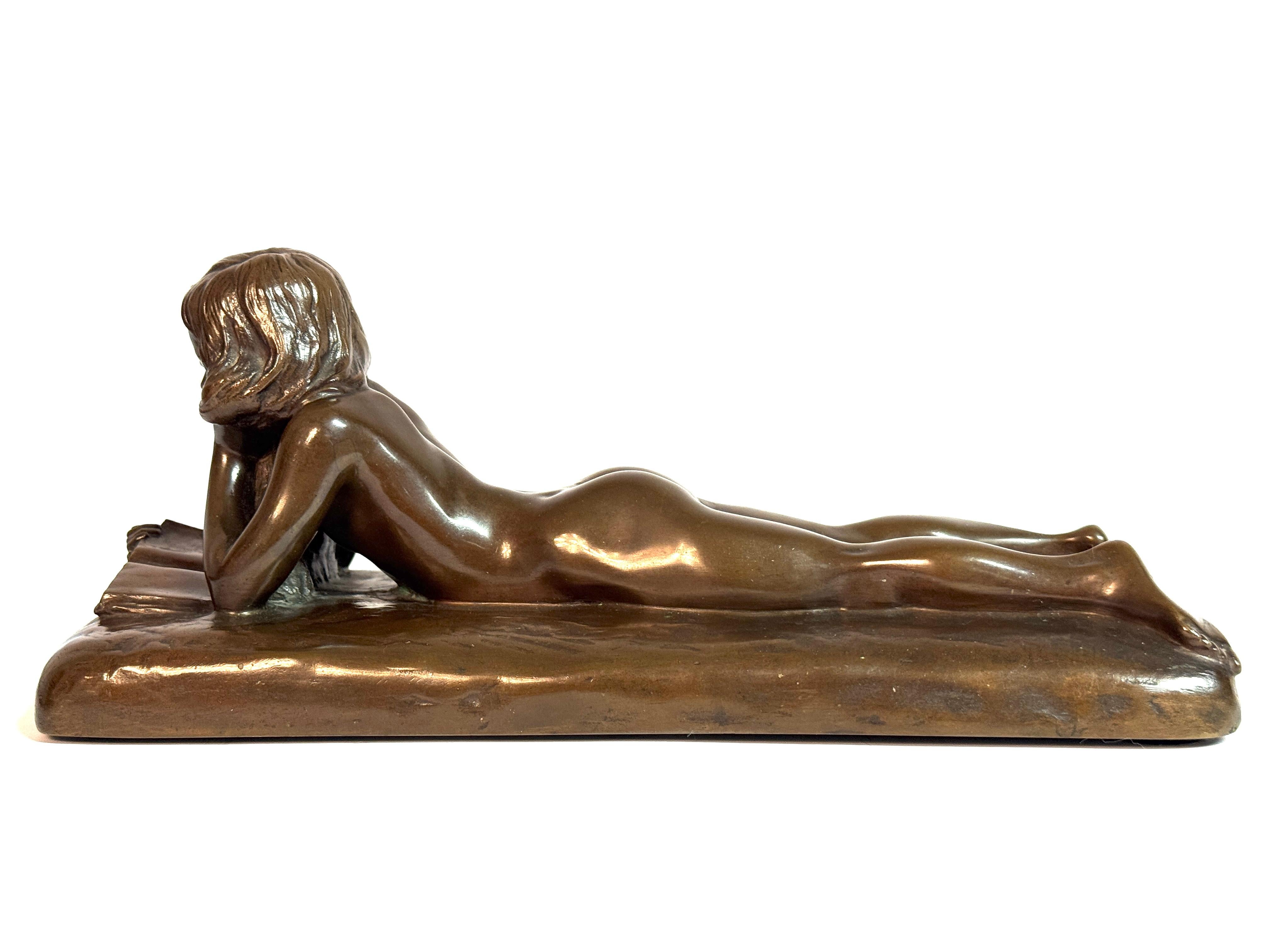 Questa elegante scultura in bronzo, firmata da Johannes Seiler, ritrae una donna nuda reclinata immersa nella lettura. Sdraiata a pancia in giù, sostiene delicatamente la testa con la mano sinistra appoggiata sulla guancia, mentre il braccio destro