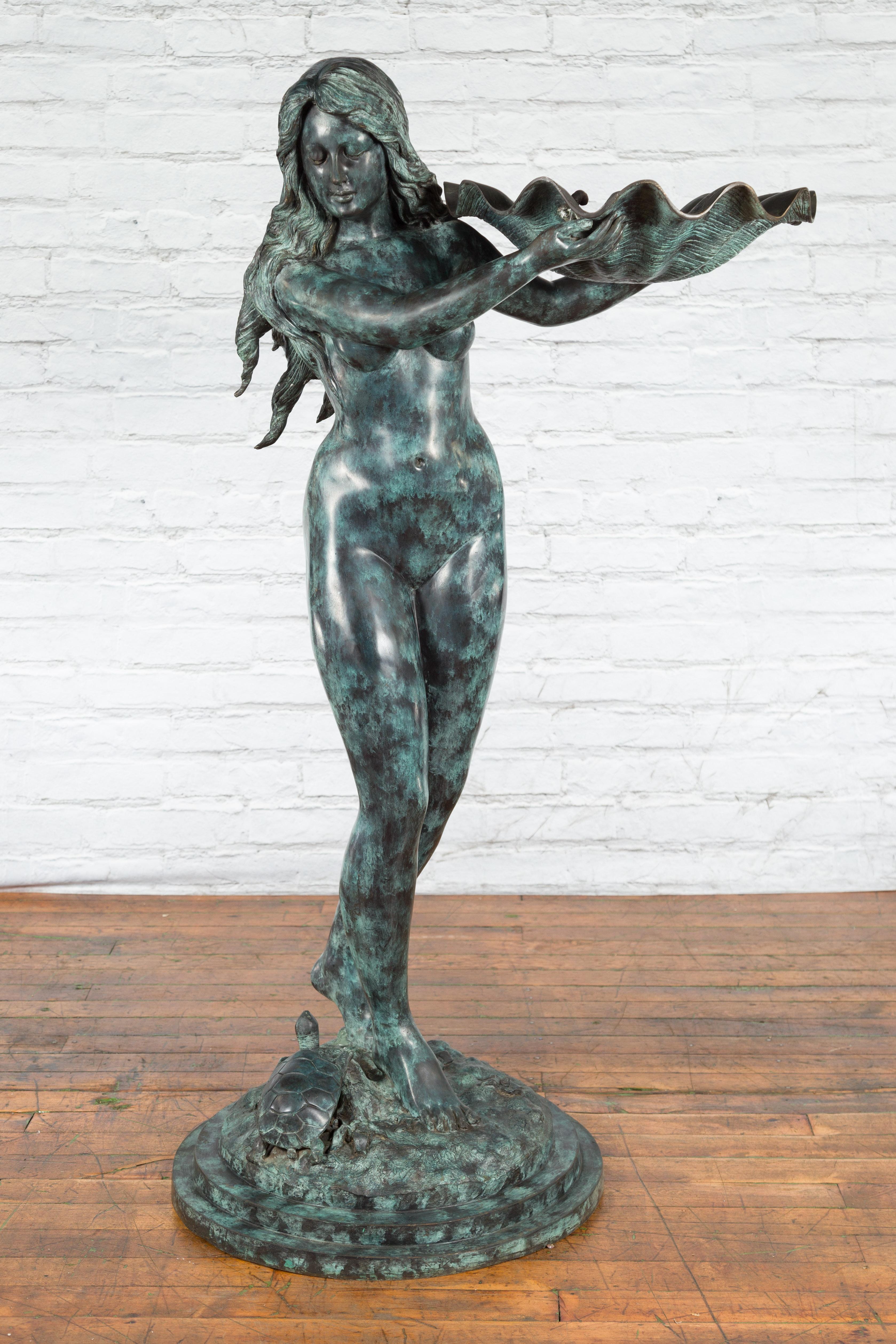 A lost wax cast bronze fountain depicting a sea nymph holding a shell, standing next to a turtle. Created with the traditional technique of the lost-wax (à la cire perdue) which allows for great precision and finesse in the details, this fountain