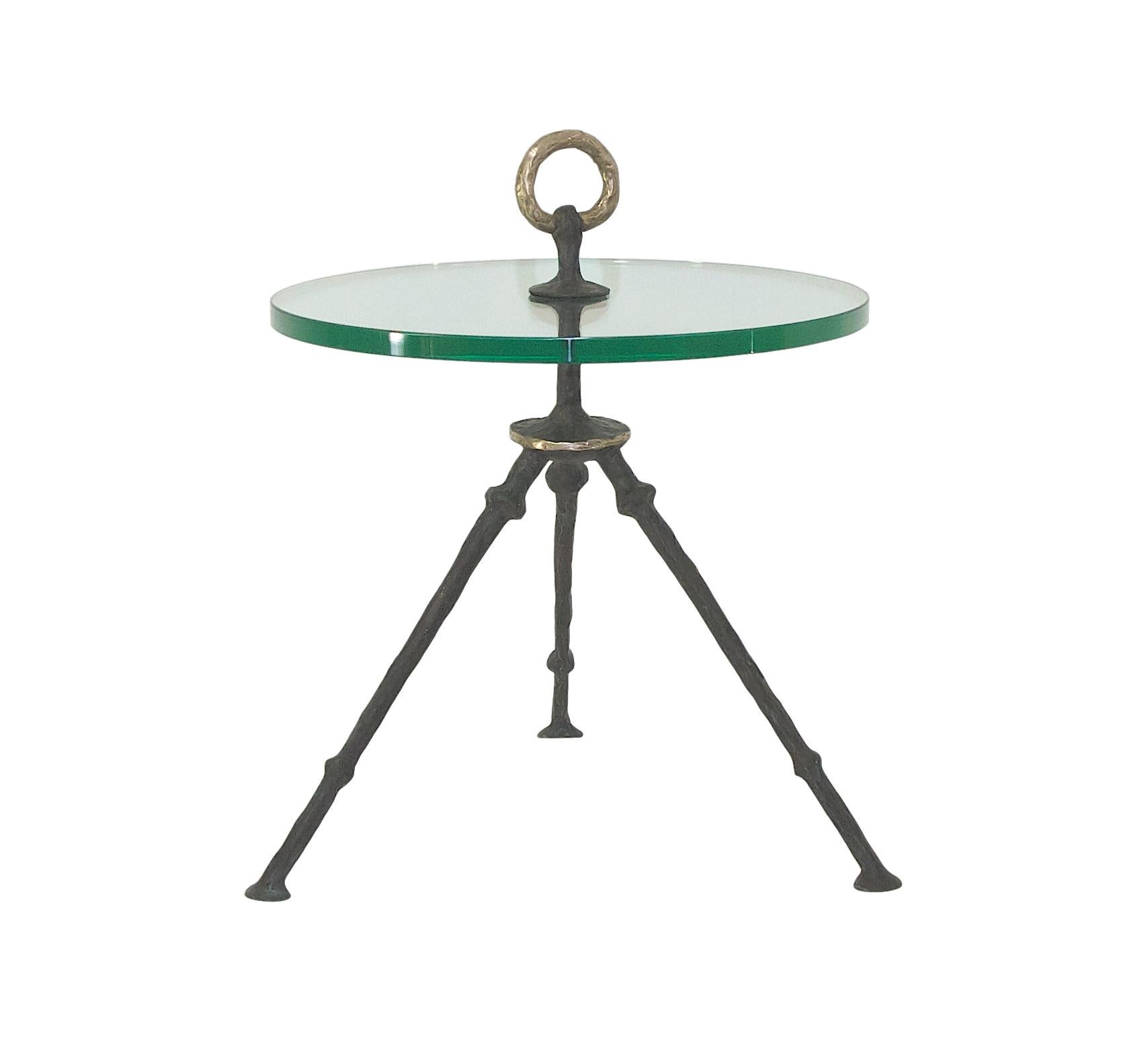 A hand-sculpted and forged tripod cocktail table with a circular glass or stone top, it is fastened with a solid bronze handle on top. Custom sizes, finishes and tops available.