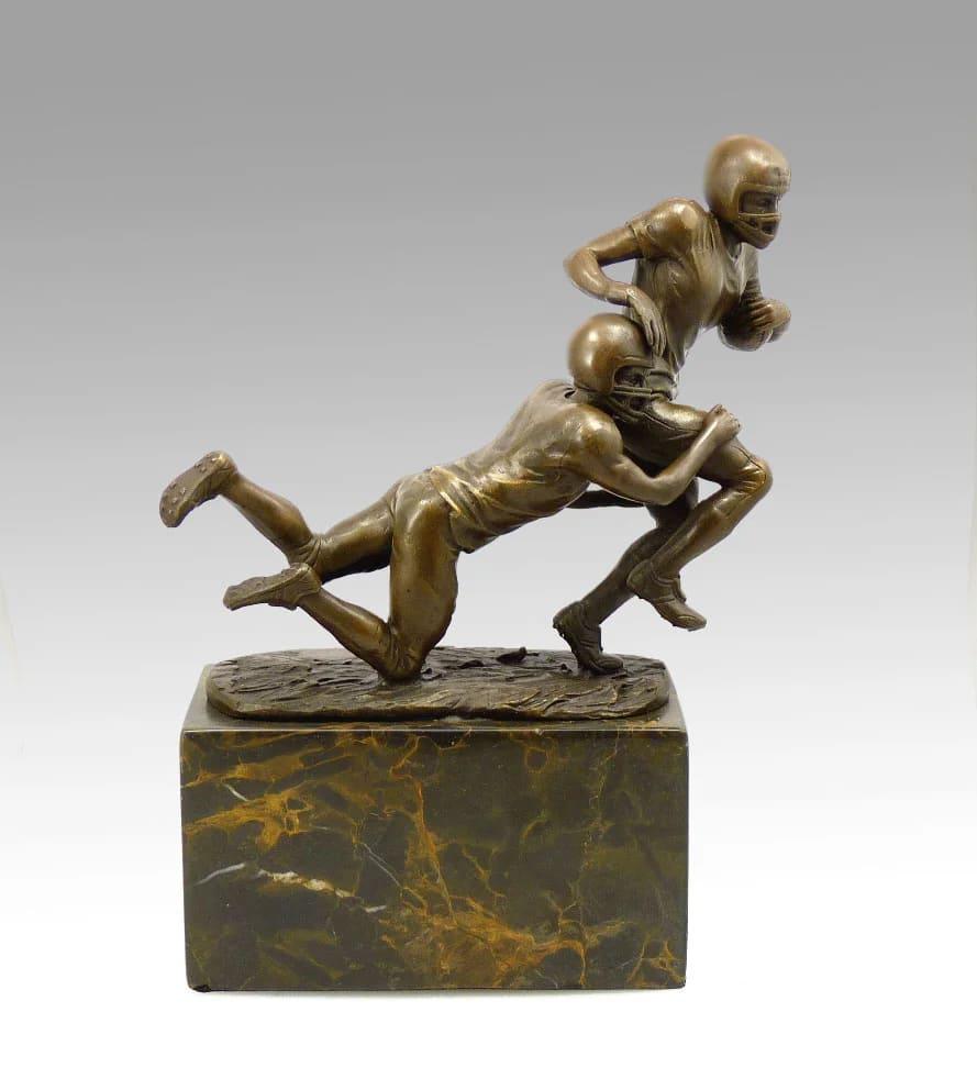 Questa statua in bronzo di un giocatore di calcio,  cattura un momento di azione in bilico, con la palla tenuta sotto il braccio del giocatore. La posizione, la definizione muscolare e l'uniforme dettagliata trasmettono forza e finezza, mentre il