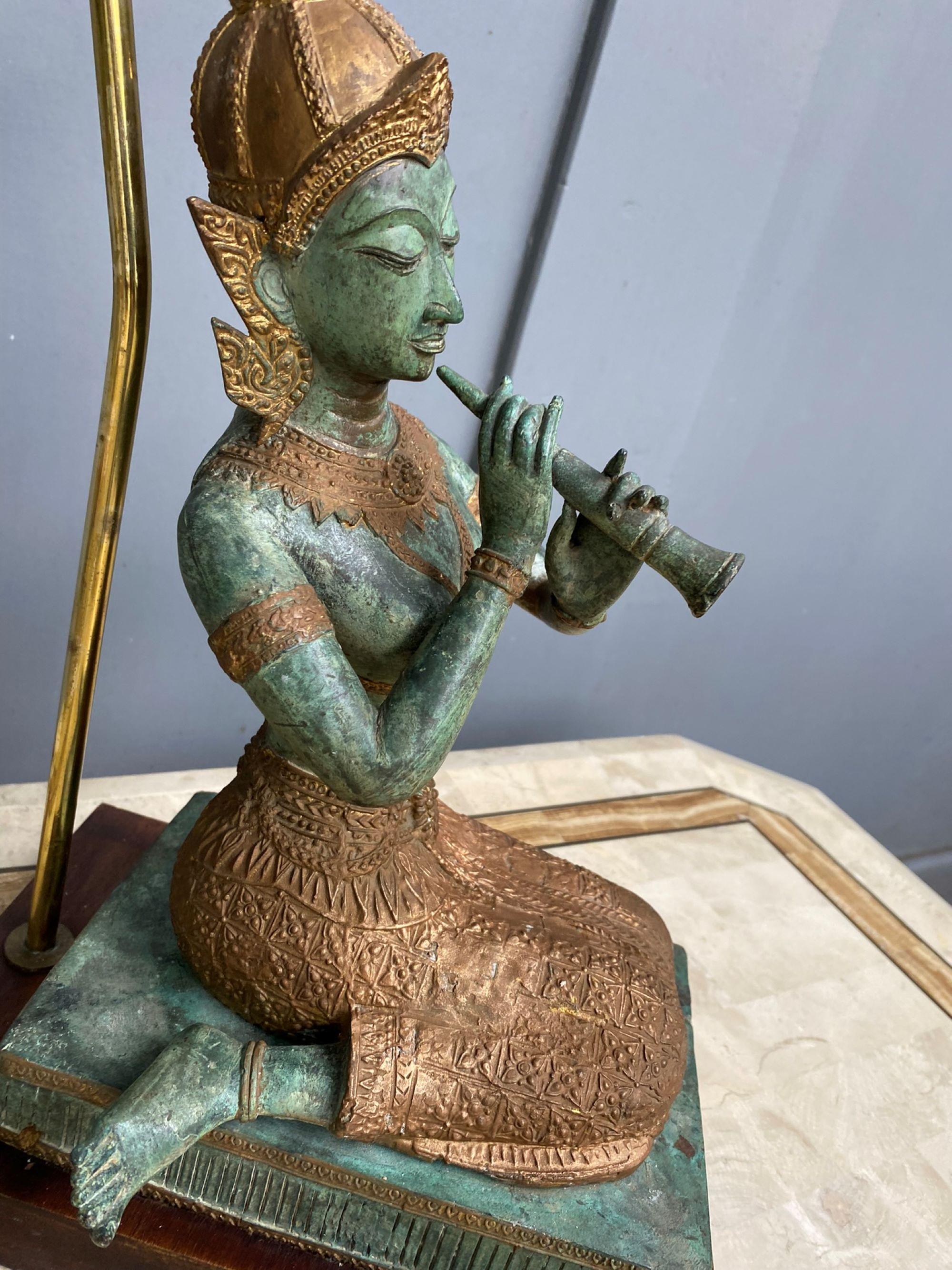 Hand cast bronze statue lamp and shade, featuring kneeling Thai angel playing a musical instrument. Sitting on a teak base, turned into a lamp, with new tapered rectangular card lampshade.

Beautiful Verdigris green finish with gold skirt, head