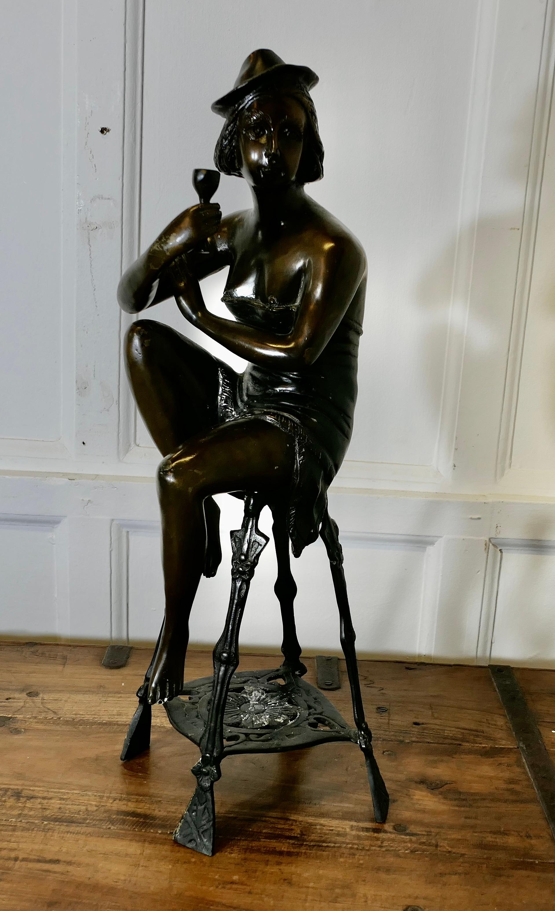 Statua in bronzo di una ragazza su uno sgabello che beve champagne 

Si tratta di un pezzo in stile anni '20, con una giovane donna un po' decadente seduta su uno sgabello da bar con un bicchiere di champagne.  in mano e un cappello piuttosto