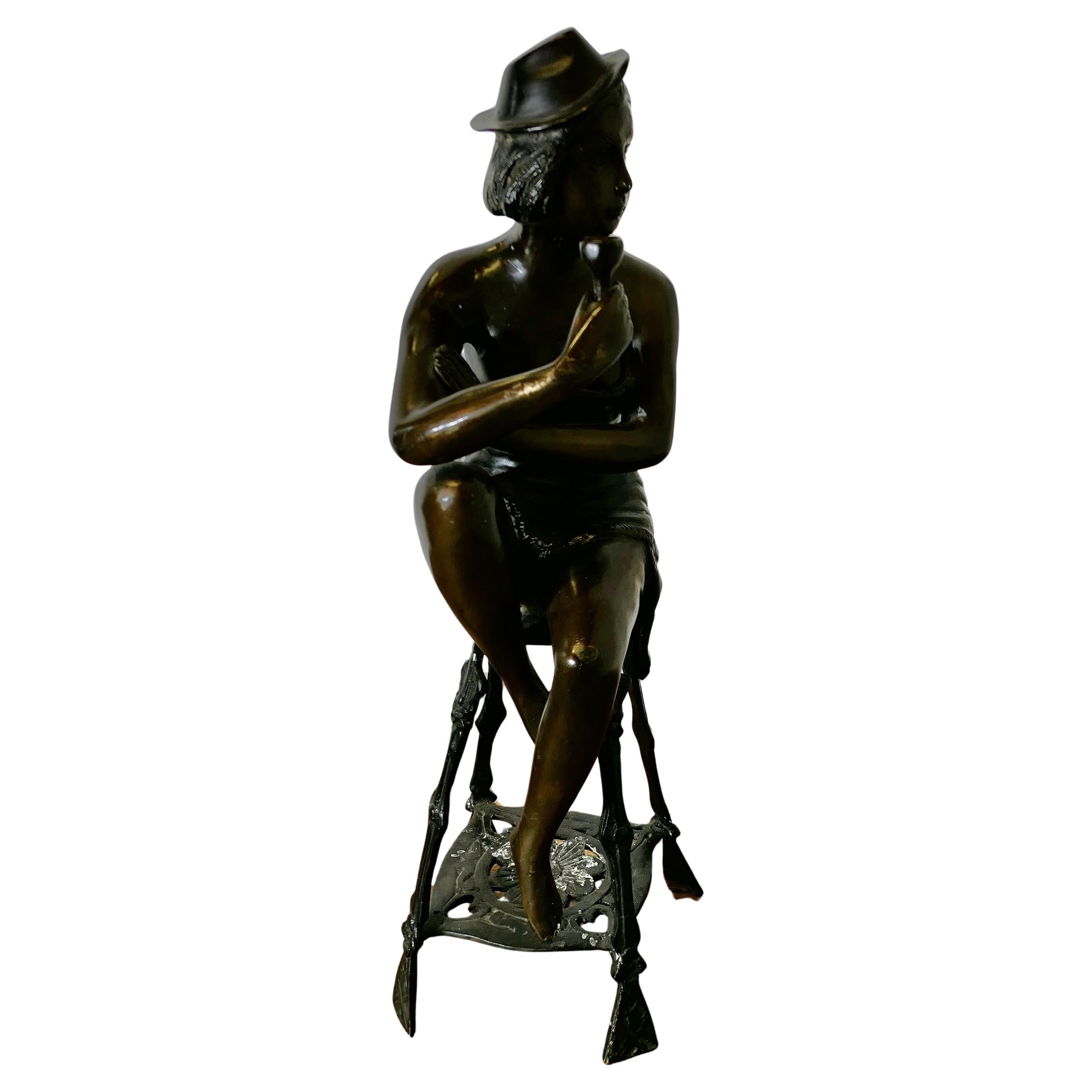 Statua in bronzo di una ragazza su uno sgabello che beve champagne