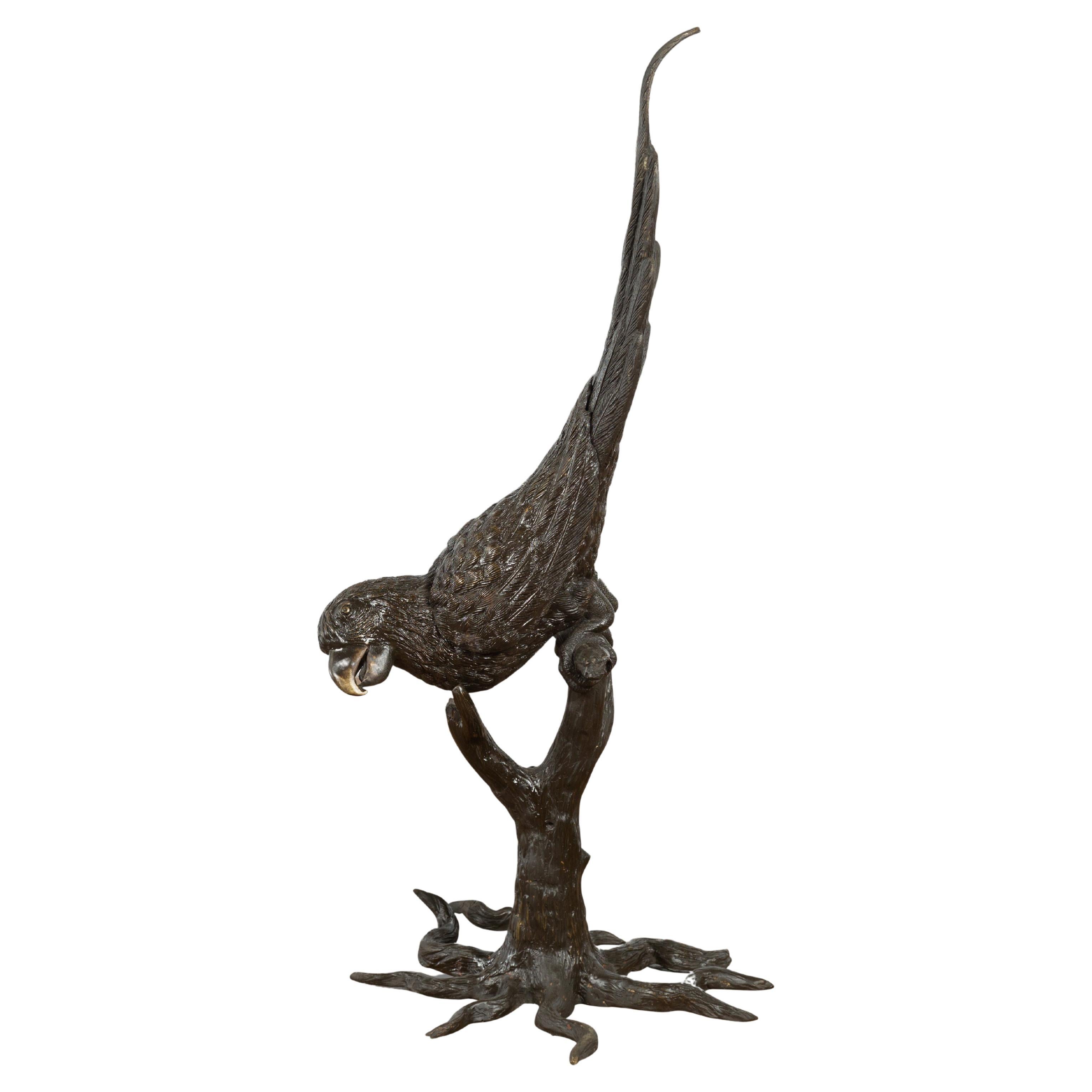 Statue en bronze d'un perroquet perché sur une branche et allongé, avec patine foncée