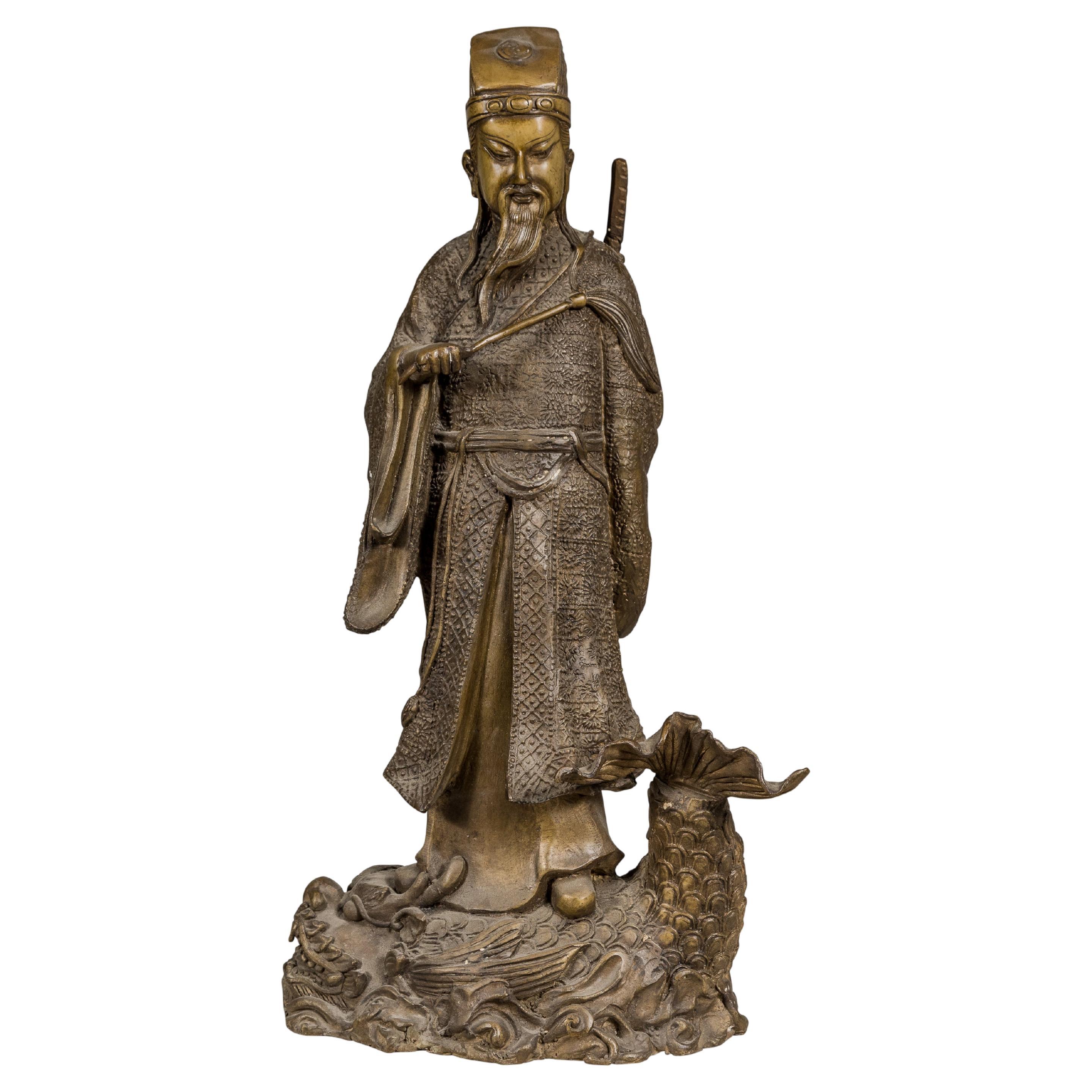 Estatuilla de bronce de una figura ancestral de pie sobre un pez gigante