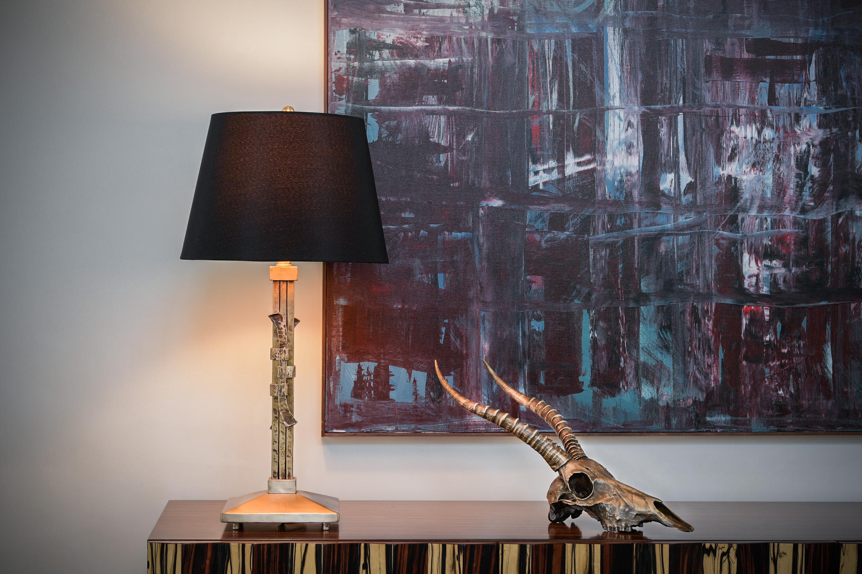 This bronze table lamp is made from solid forged bronze bars that have been grouped together utilizing a traditional Japanese joinery technique. The bronze bars have been lightly hammered to add texture and come to rest on a slightly graded and