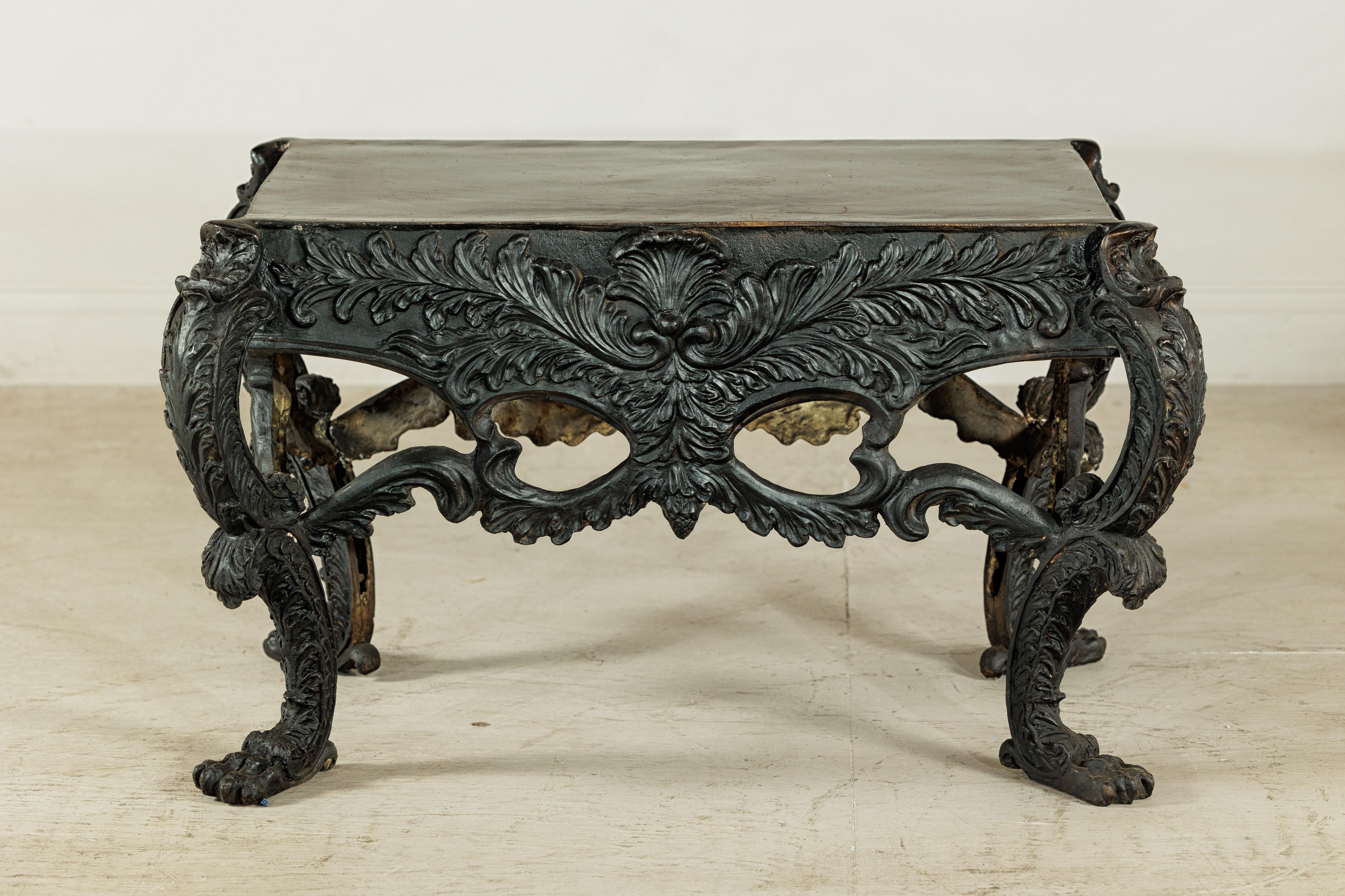Esta llamativa mesa de bronce se define por su presencia escultural y su diseño ricamente detallado. La parte superior rectangular de bronce descansa sobre una ornamentada base de fundición adornada con hojas de acanto enrolladas, motivos de concha