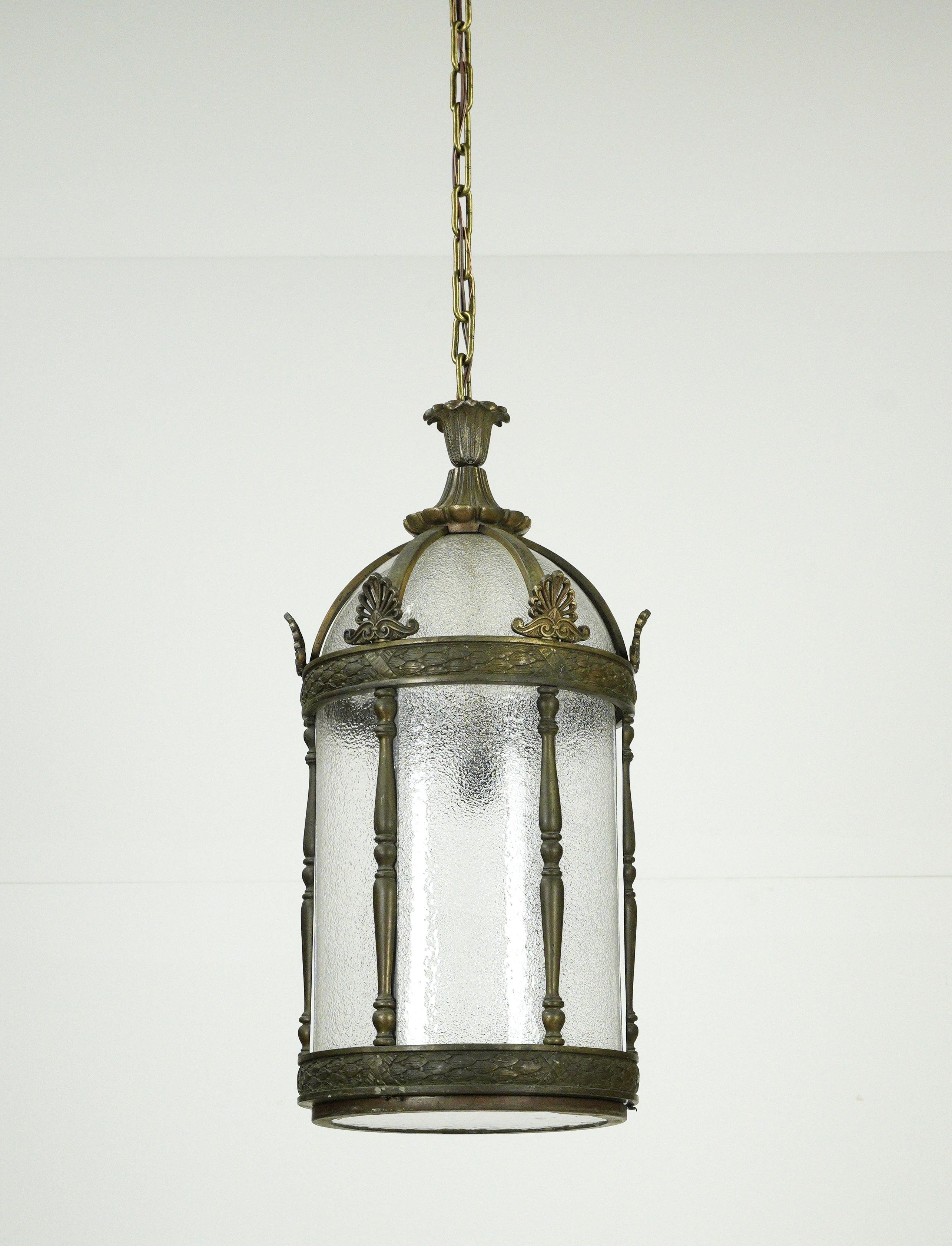 Large solid bronze framed pendant lantern with clear textured glass and a steel chain. Cleaned and restored. This light requires one single standard light bulb. Indoor use only. Good condition with appropriate wear from age. This light is wired and
