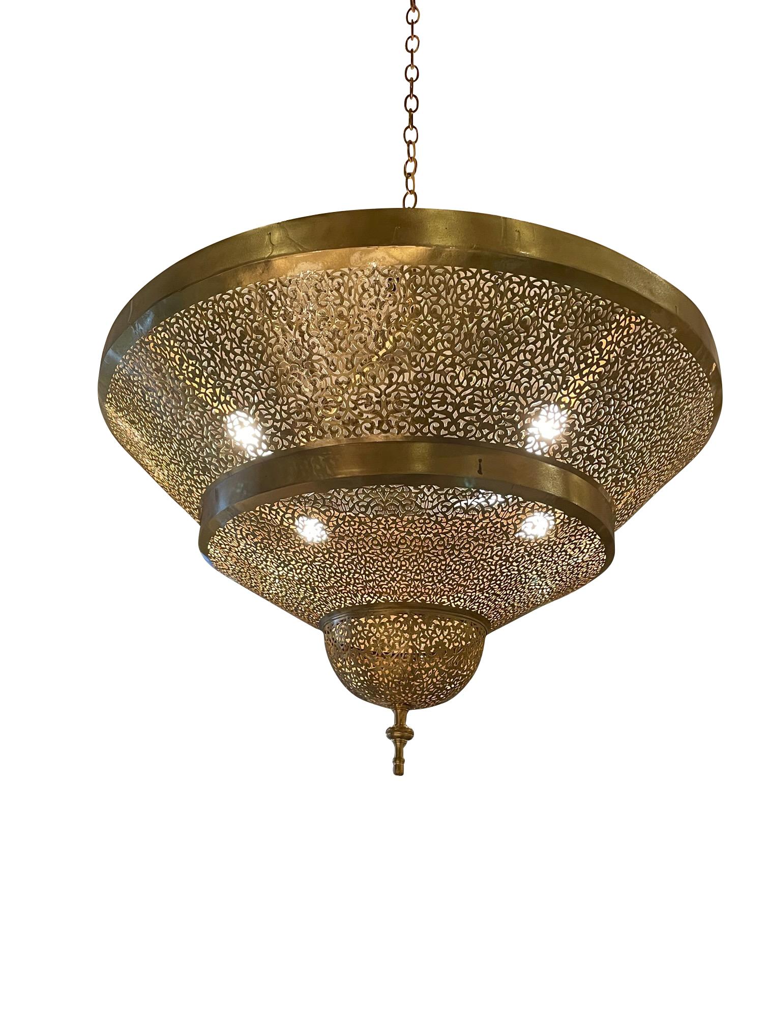 Contemporary Moroccan three tiered bronze chandelier.
Decorative perforated design.
Four candelabra bulbs.
Finial bottom.
Fixture OH 18