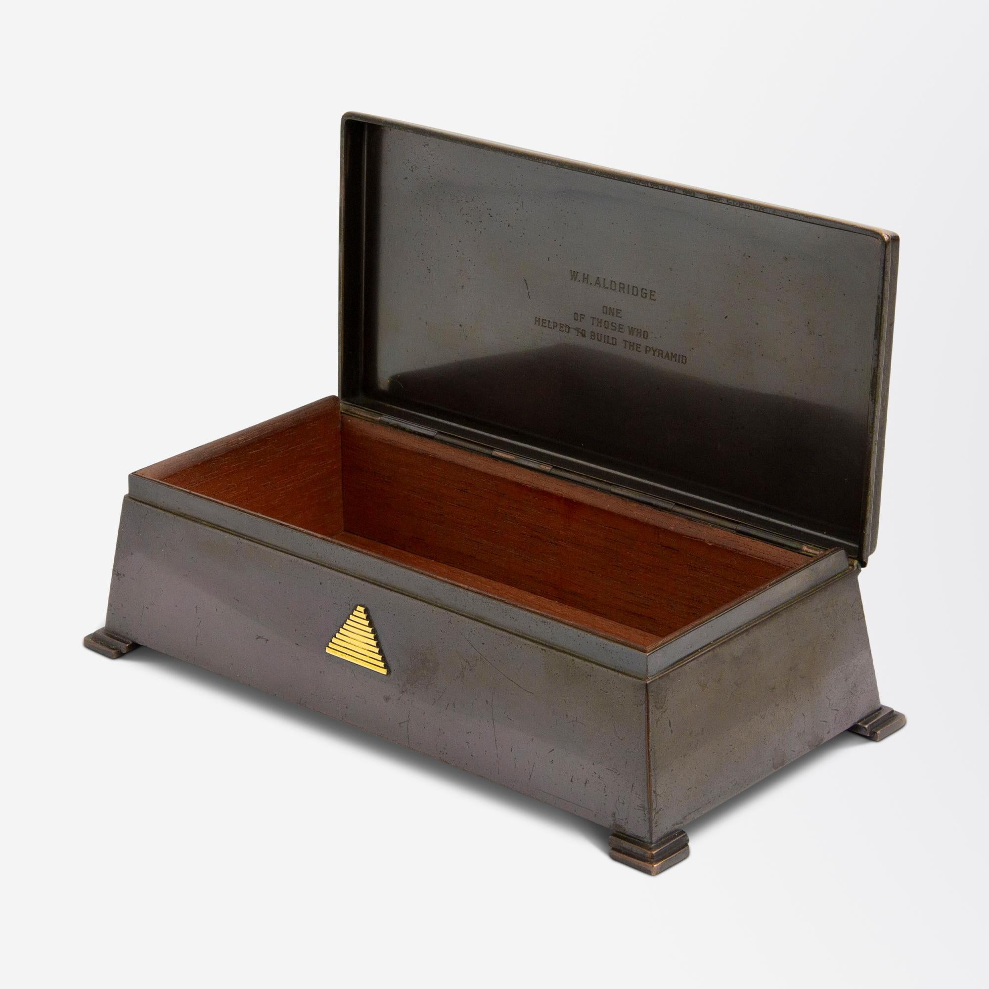 An anodised bronze, cedar-lined box, by Tiffany & Company dedicated to Walter Hull Aldridge, circa 1945. The box has four stepped feet in each corner, and is decorated with 18 karat yellow gold accents – on the front is a pyramid, and on the lid is