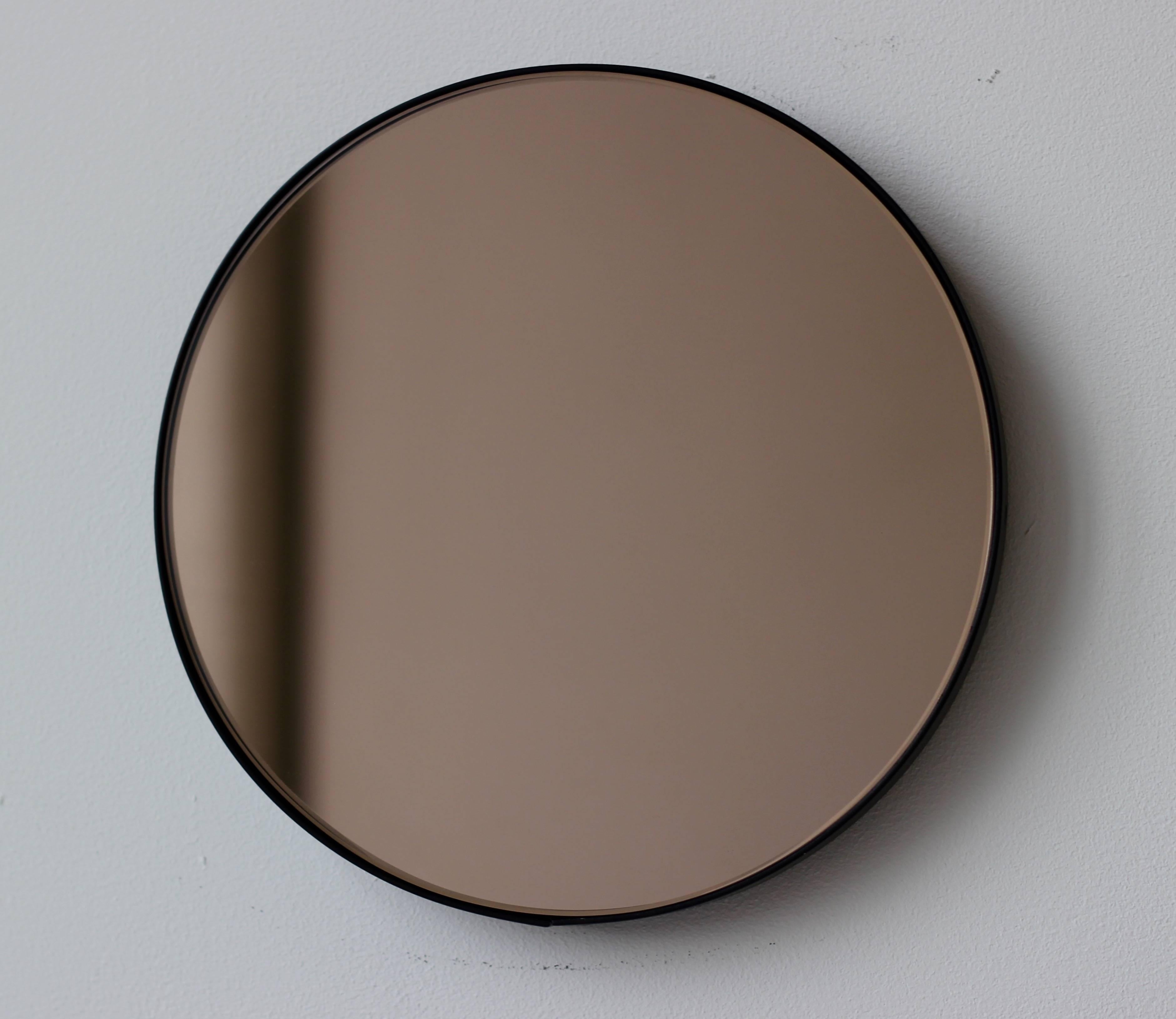 Zeitgenössischer Orbis™ runder, bronzefarben getönter Spiegel mit einem minimalistischen, schwarz pulverbeschichteten Aluminiumrahmen. Entworfen und handgefertigt in London, UK.

Die mittelgroßen, großen und extragroßen Spiegel (60, 80 und 100 cm)
