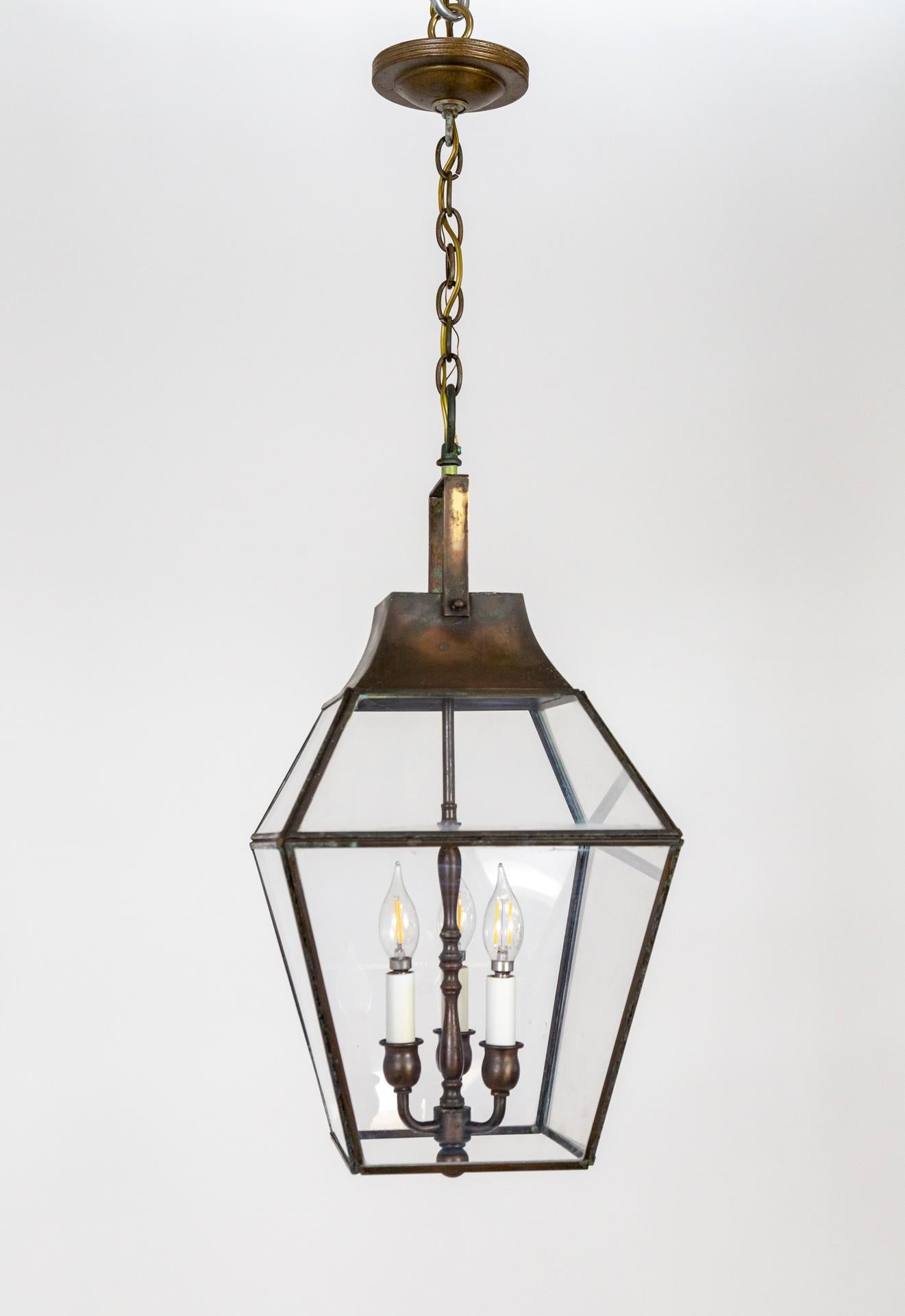 A geometric copper lantern with a bronzed finish, plexiglass windows, and 3 candelabra lights held inside by a turned-style stem; topped with a cap and handle.  With new candle covers, chain, and canopy. Newly rewired. 11.5