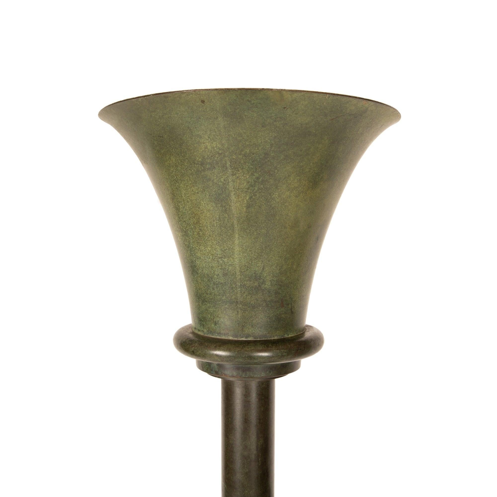 Una antorcha de bronce con tres portaflores cónicos ajustables y una repisa redonda de vidrio fundido.