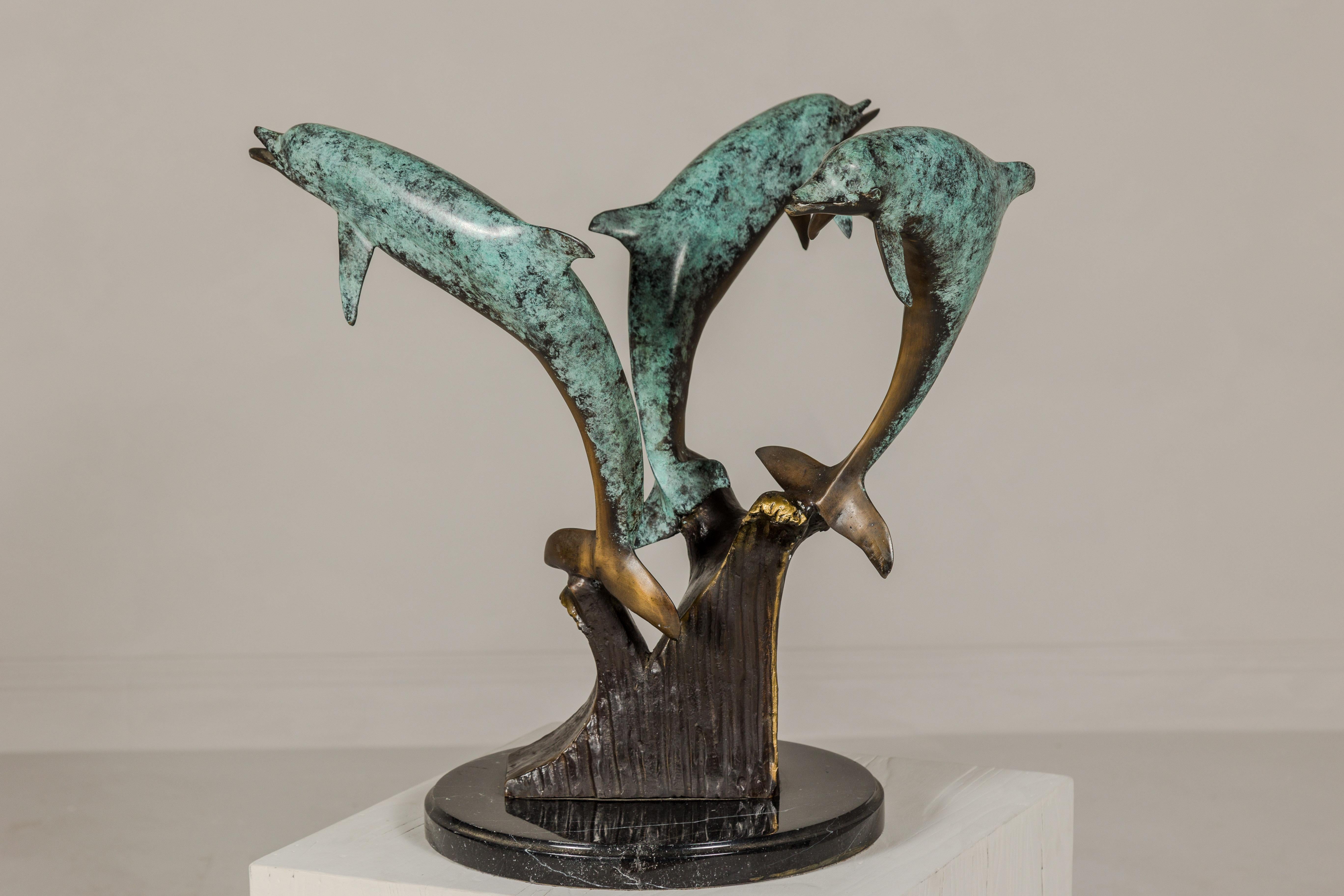 A bronze triple dolphin table base sculpture with black marble stand. Adorn your home with the captivating beauty of the sea with this exquisite bronze triple dolphin table base sculpture. Its intricate design and mesmerizing verdigris patina will
