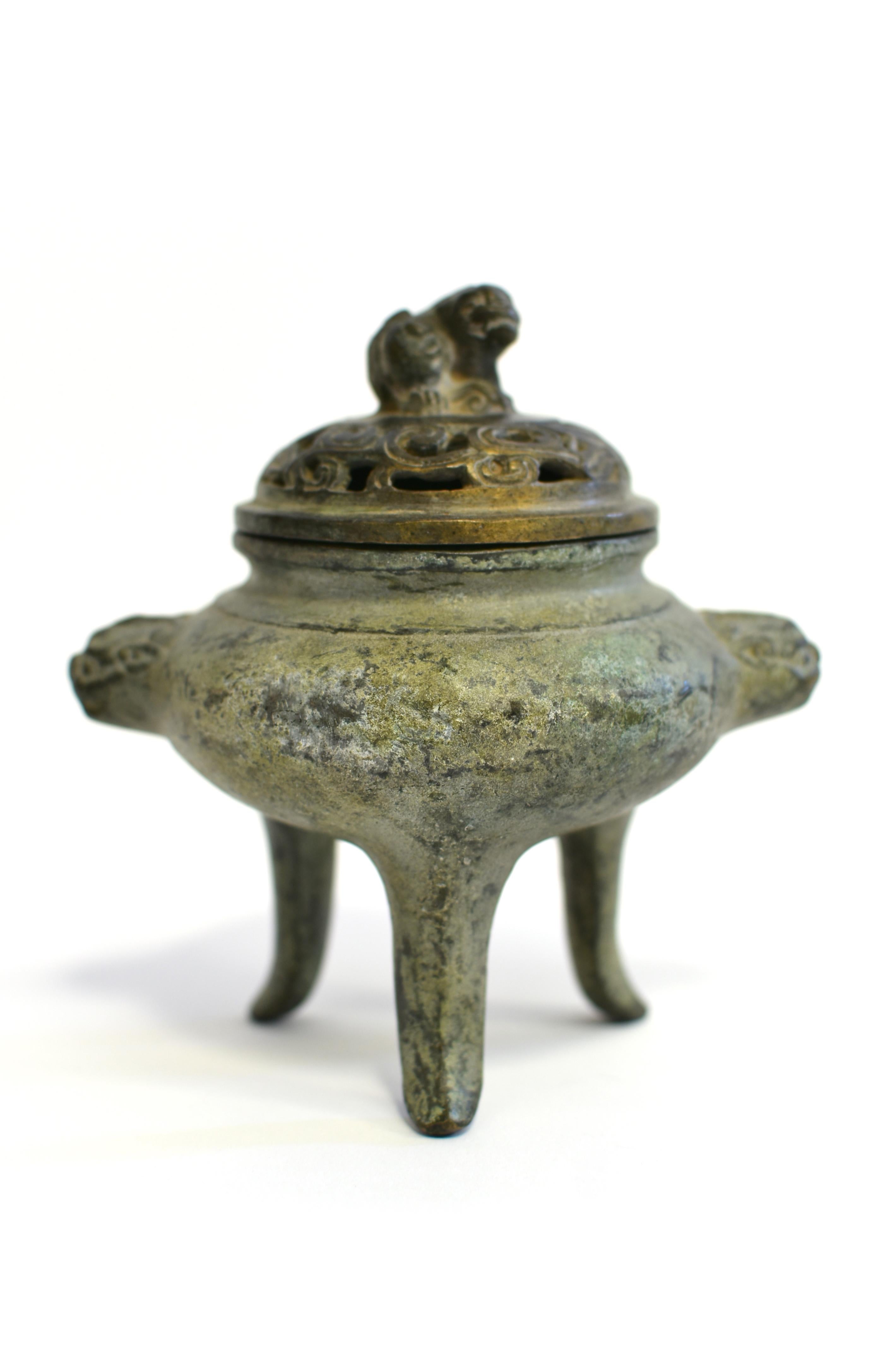 A beautiful antique bronze incense burner in the Ming dynasty style. The vessel's bulbous sides are free of decorations, flanked by a pair of foo dog lions with ferocious expression. The cover is pierced with a scroll and chrysanthemum design,
