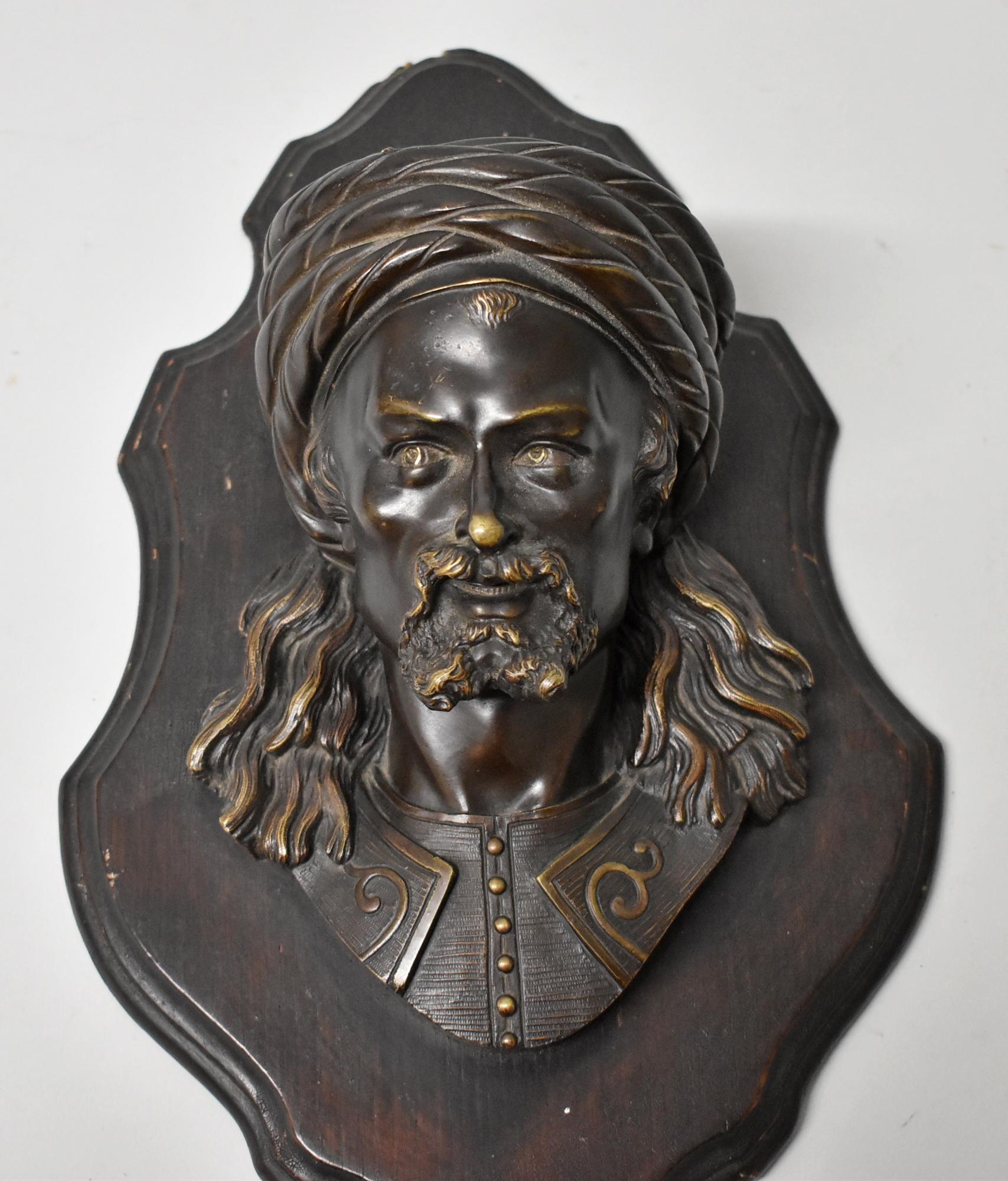 Plaque murale en bronze représentant une tête d'homme, estampillée LeBlanc. Homme arabe avec des poils au visage et un turban. Le buste est monté sur une planche de bois. Il y a un espace entre la statue et la plaque qui peut être utilisé comme