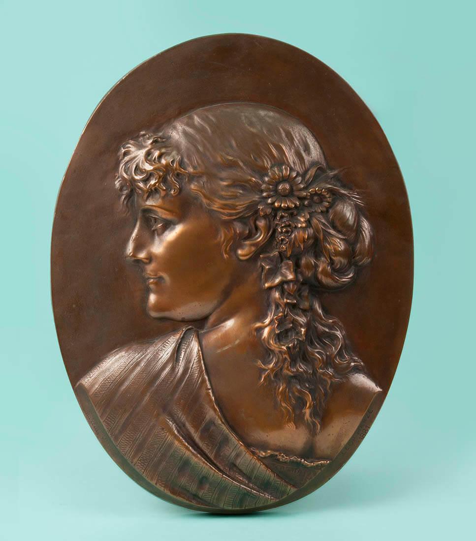 Elegant wall plate or medal, depicting a young lady with flowers in her hair. 
Romantic style, dated 1881. 
The bronze is signed and made by Léopold Harze. 
This artist was educated at the school of art in Liège, Belgium, between 1845 and 1854.