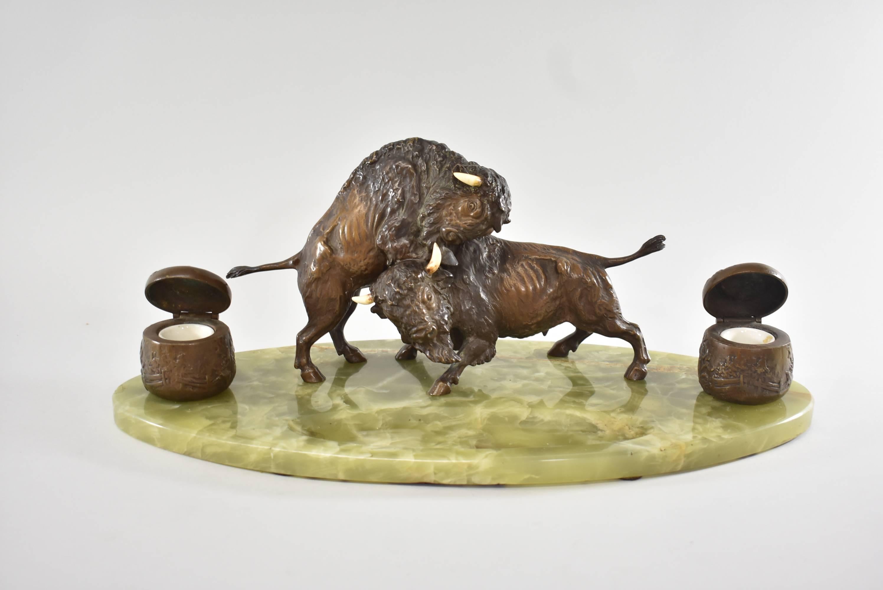 Western inkwell features two cast highly detailed bonze fighting buffalos set on an oval green onyx base with carved out pen rest. The inkwells are embossed with a fenced pastural scene and hold porcelain removable inserts. Nice rich patina. Chip on