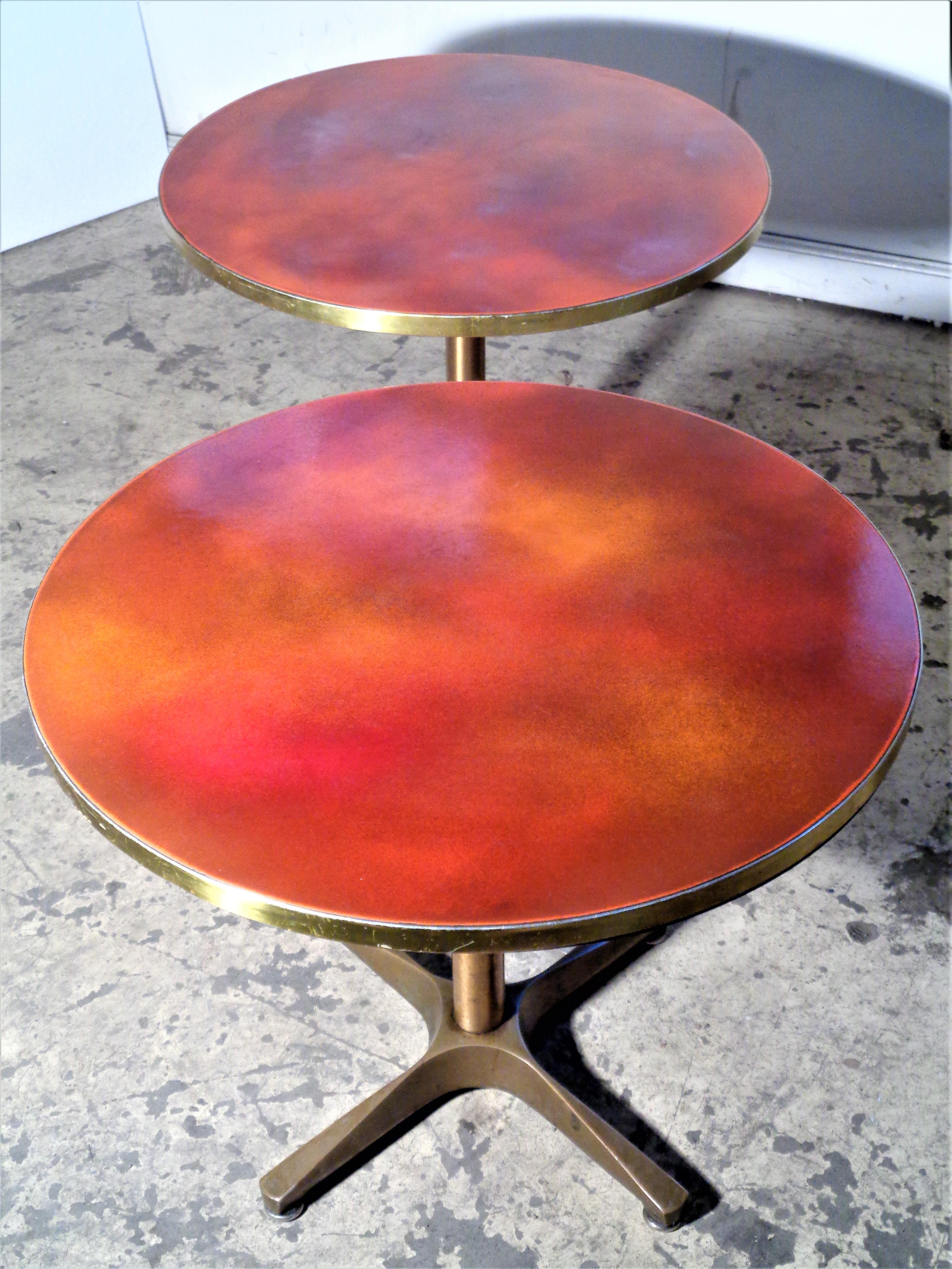 Industrial quality bronze and iron x base adjustable height pedestal tables with brass trimmed brilliant variegated orange enameled tops. The circular tops lock into place lock by spinning tops to the right and they will swivel by spinning the tops