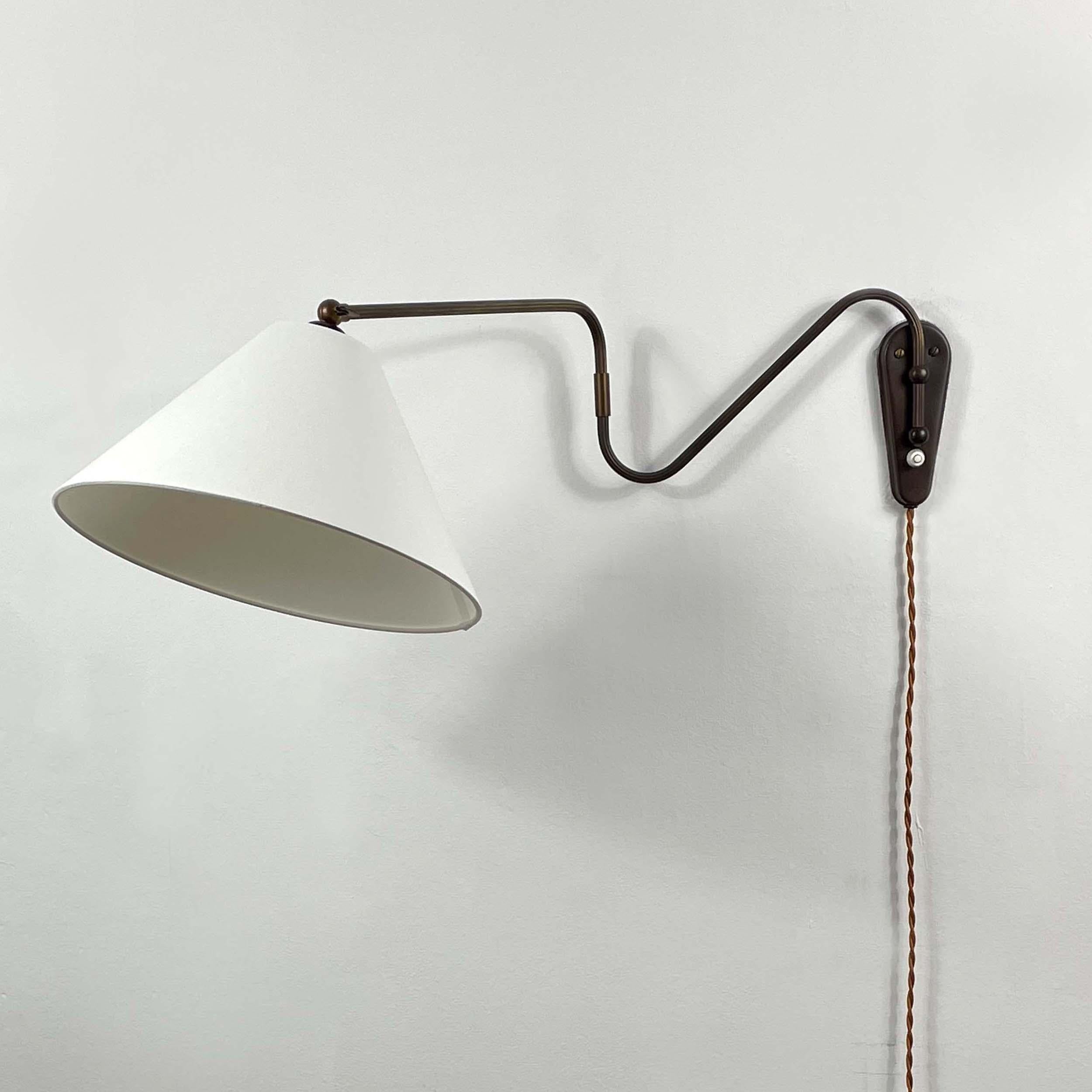 This unusual 1950s adjustable and articulating vintage wall light was designed and manufactured in Sweden.

The lamp features an off-white fabric lampshade and bronzed brass articulating lamp arm with brass details. The lamp has been rewired with