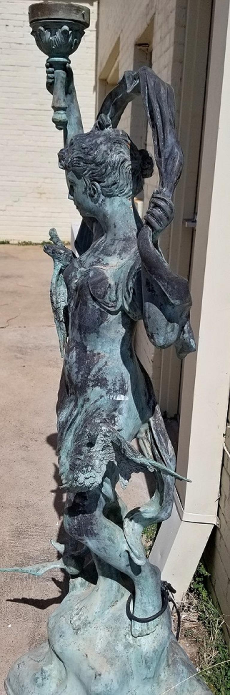 Presenting a lovely vintage piece of garden statuary or architectural salvage.

This is an impressive bronzed metal statue/figure of a lady holding a torch in the right hand and a billowing scarf in the left hand. She is surrounded or flanked by