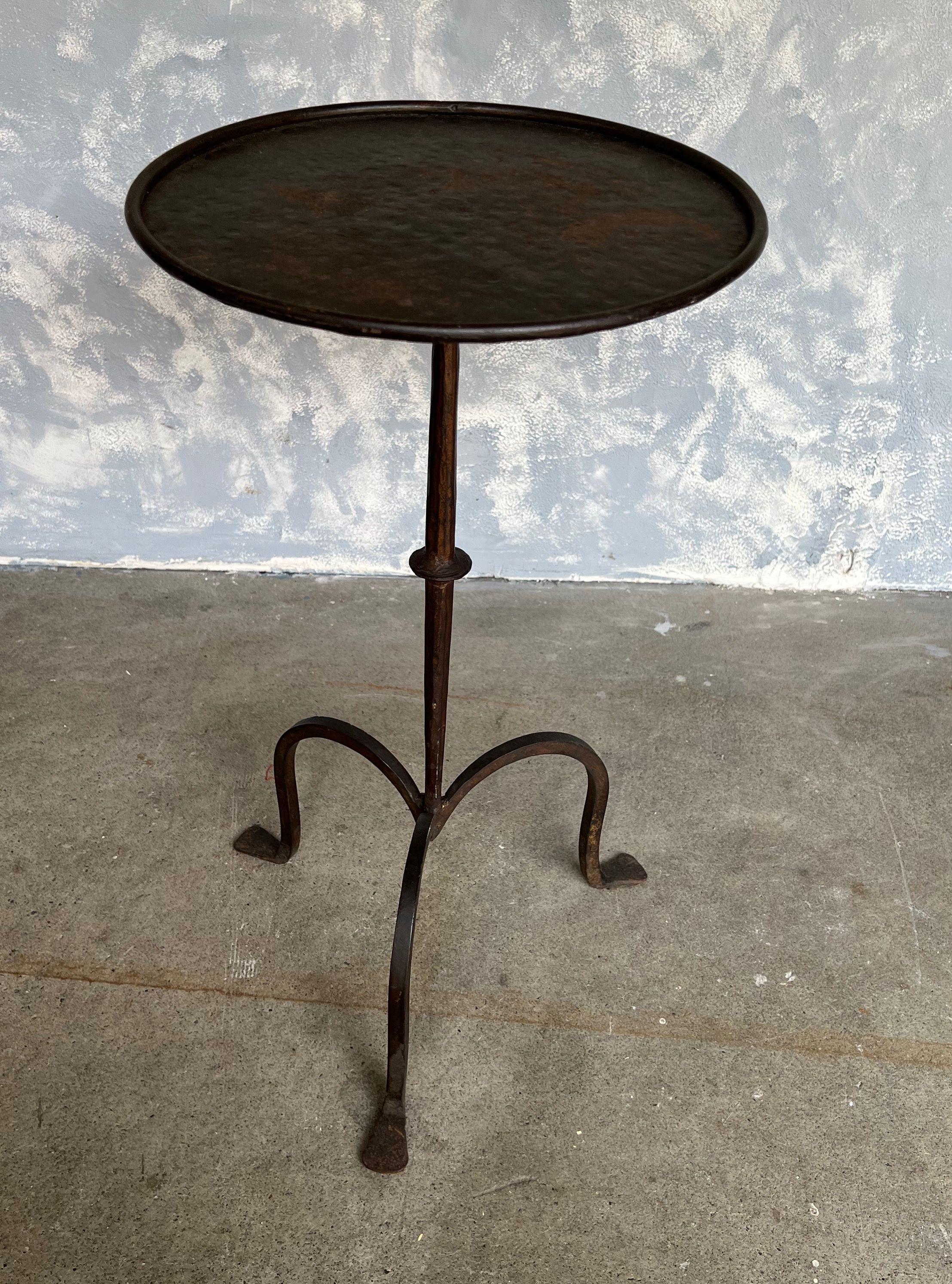 Lovely iron and metal end table with a footed tripod base, a central ring detail on the stem, and a ring surround at the top. Perfect for a drink, it can easily be moved around as needed. Beautiful bronzed patina. 

Spanish, 1950s. Very good