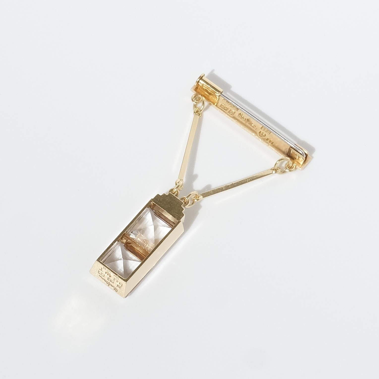 Cette broche en or 18 carats de style Art déco comporte un pendentif en forme d'escalier qui retient deux cristaux de roche carrés à facettes. Les lignes géométriques, les coupes nettes, le design moderne et les cristaux de roche à facettes carrées
