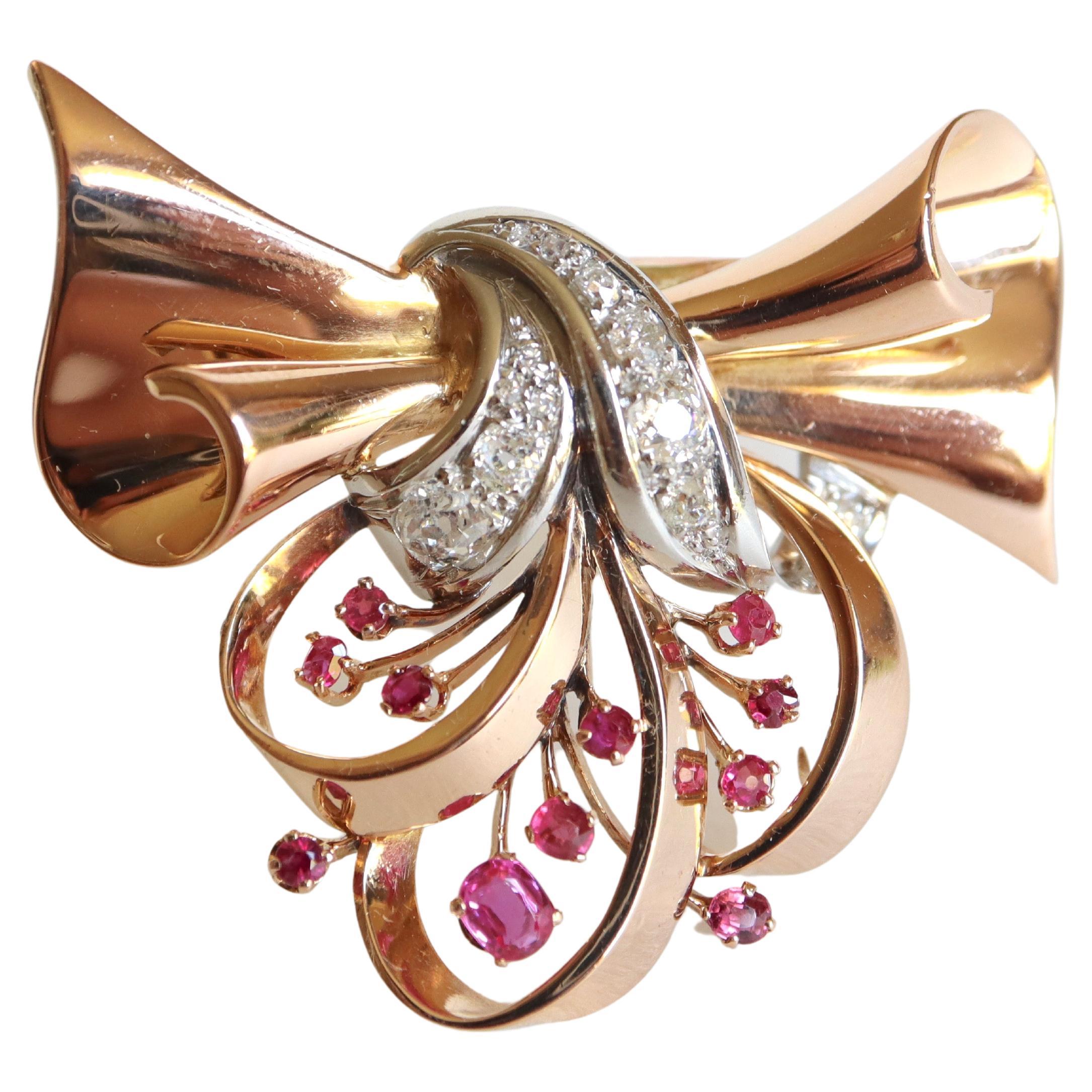 Spilla da bavero a forma di nodo movimentato in oro giallo 18 carati e platino, ornata da diamanti per un totale di circa 0,60 carati e 14 rubini di varie dimensioni.
Bellissimo gioiello elegante degli anni '40. Spilla a forma di nodo movimentato in