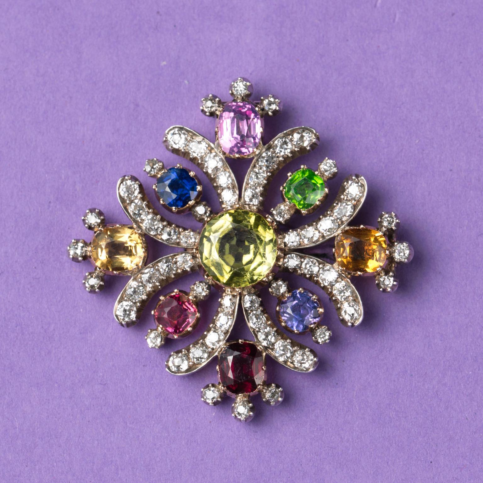 A Georgian brooch in the shape of a Maltese cross in silver with gold backing and open-set gemstones (peridot, sapphire, citrine, demantoid and almandine garnet, and spinel); the geometric curved lines are set with old-cut diamonds. A double usage,