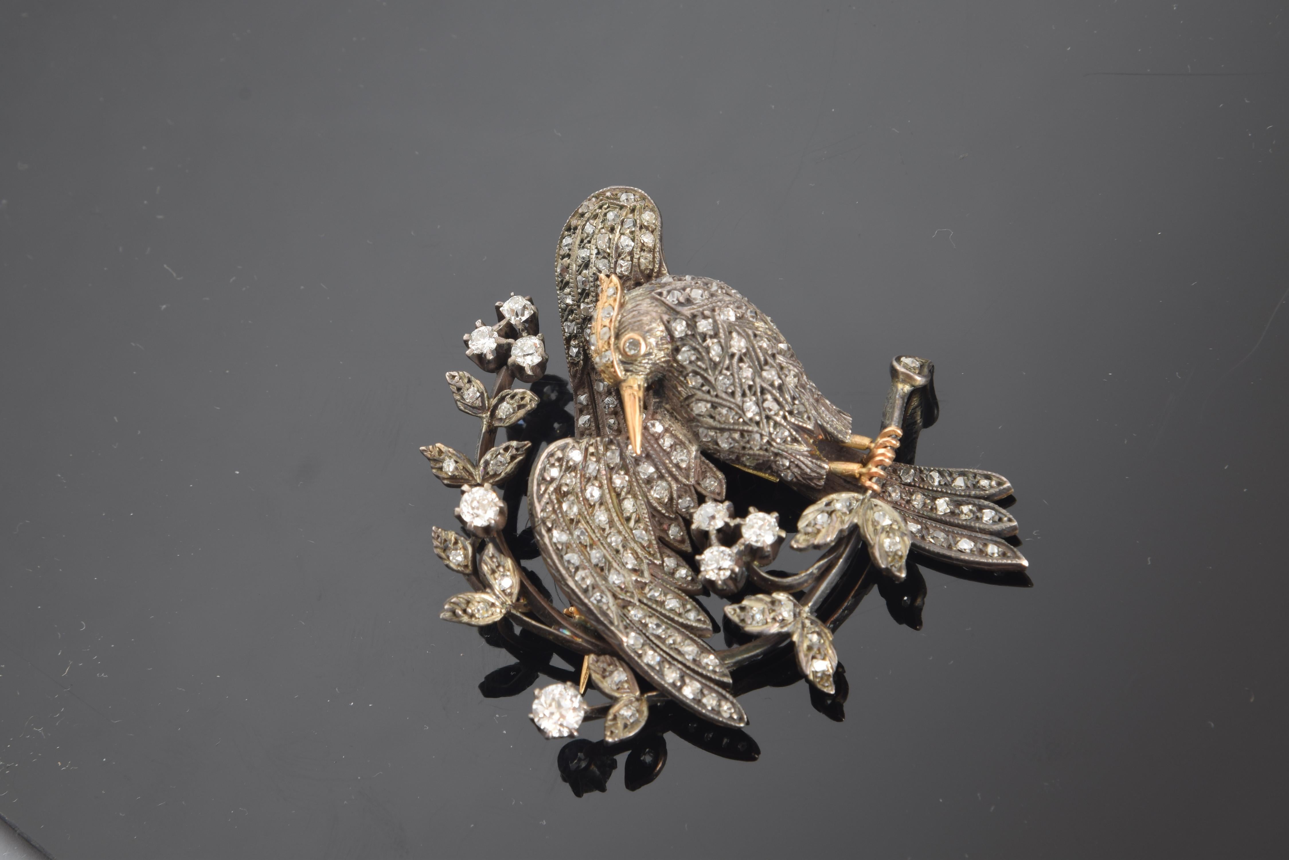 Gold and white gold and brilliant cut diamonds.
It has been represented in this jewel a bird perched on a branch with flowers and leaves, preening a wing with the other also extended. It is made in white gold and that same metal in its color, and