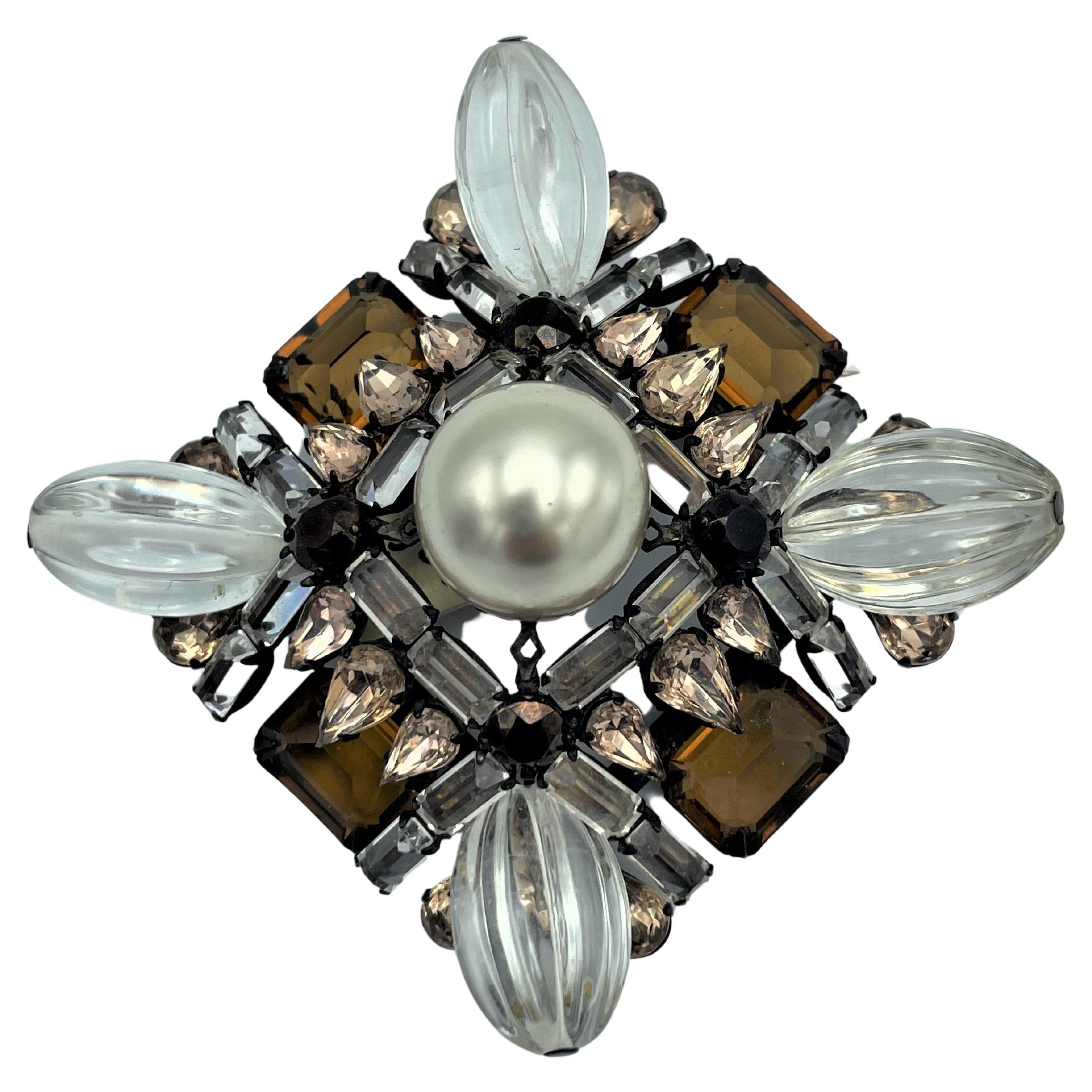 About

Henry Schreiner's brooch has a square shape and is built on 3 levels. The crowning glory is a 2 cm handcrafted pearl. In between different topaz colored rhinestones in different shapes and sizes. 4 clear elliptical forms protrude from he