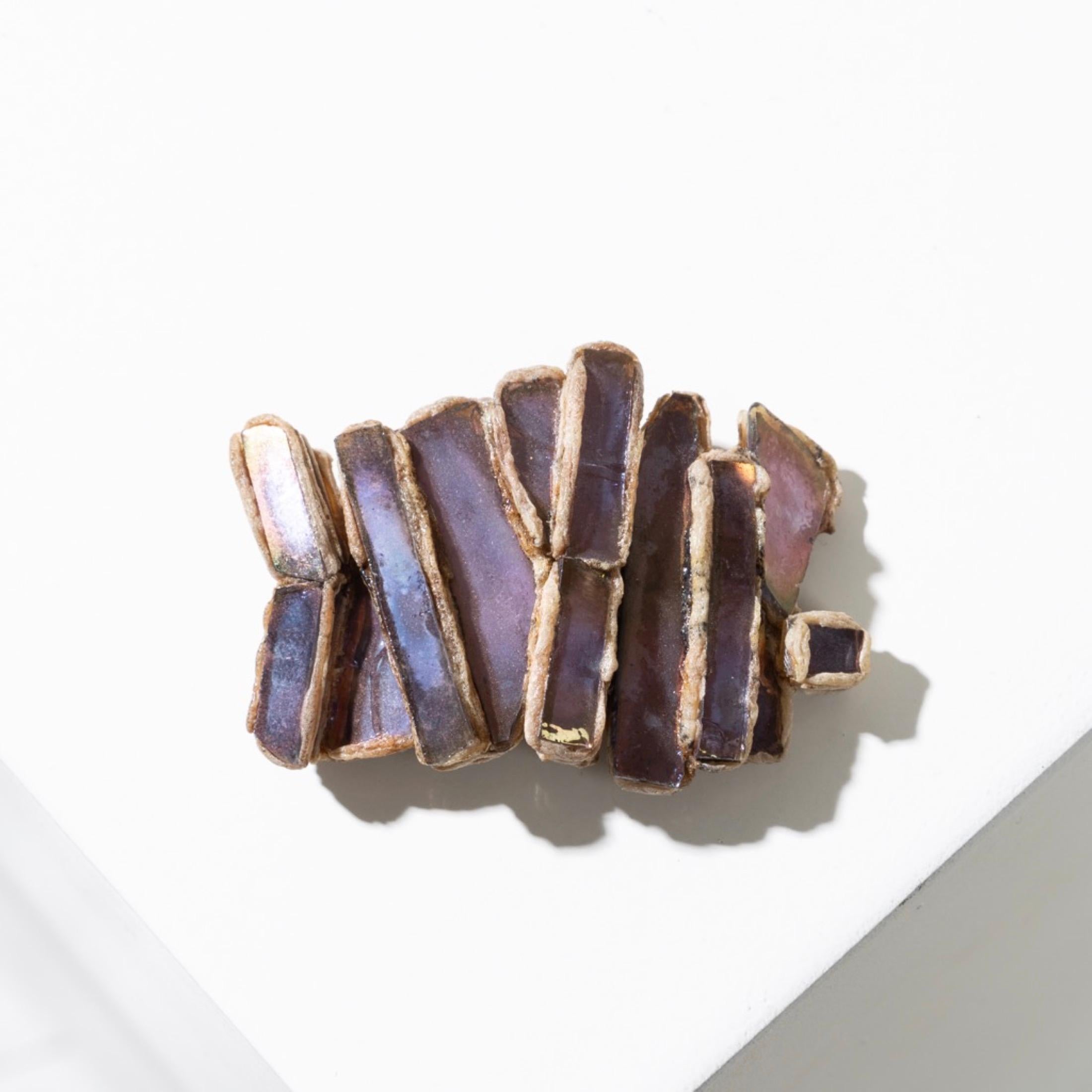 This brooch by Line Vautrin is distinguished by its elegance and refinement, thanks to the inlay of rectangular purple mirrors arranged vertically. This arrangement creates a singular rectangular shape, with multiple reliefs. The texture of beige