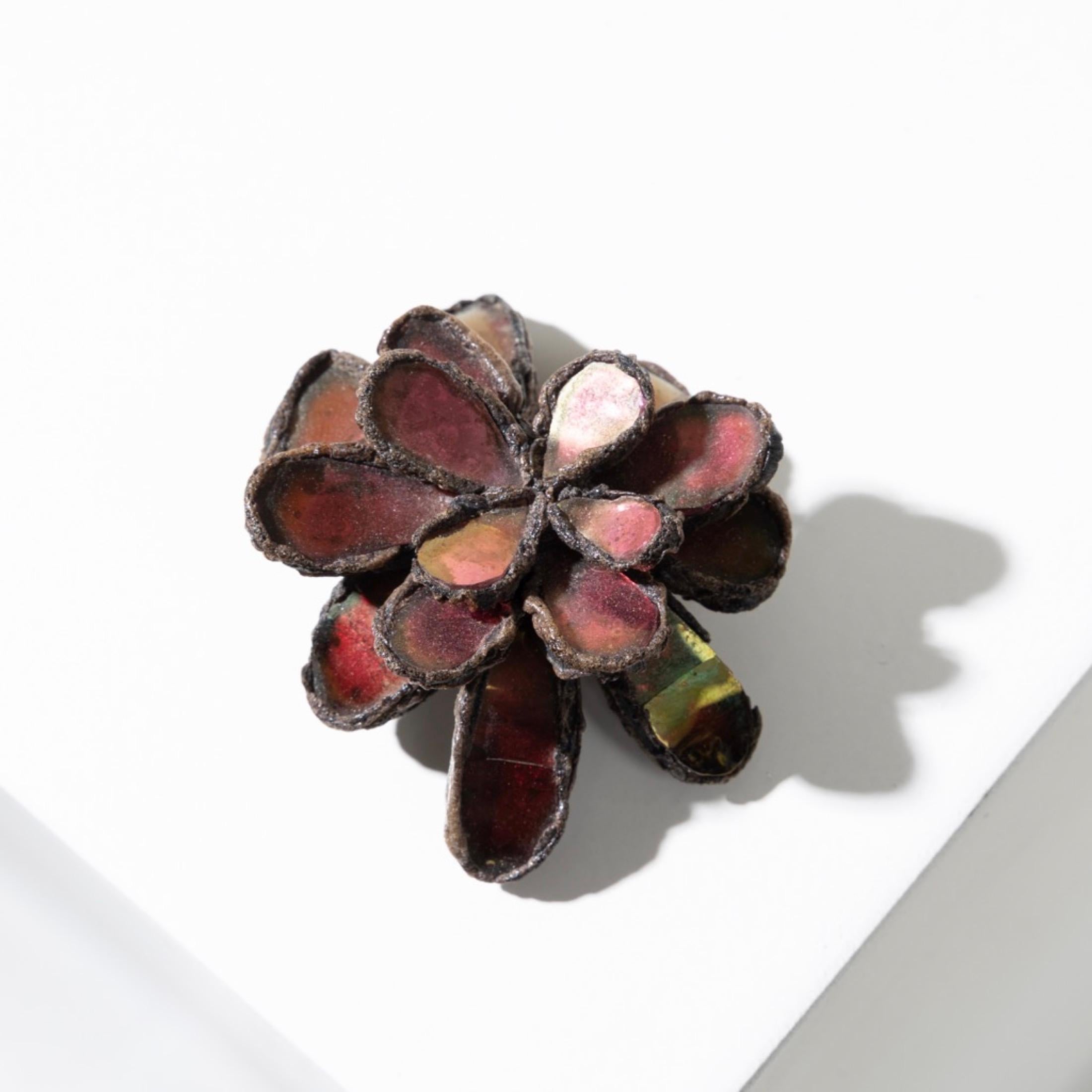 This Brooch in black Talosel encrusted with red mirrors in the shape of flower petals represents a very characteristic aesthetic of the work of Line Vautrin.
This organic shape is designed to evoke a flower, with delicately arranged red mirrored