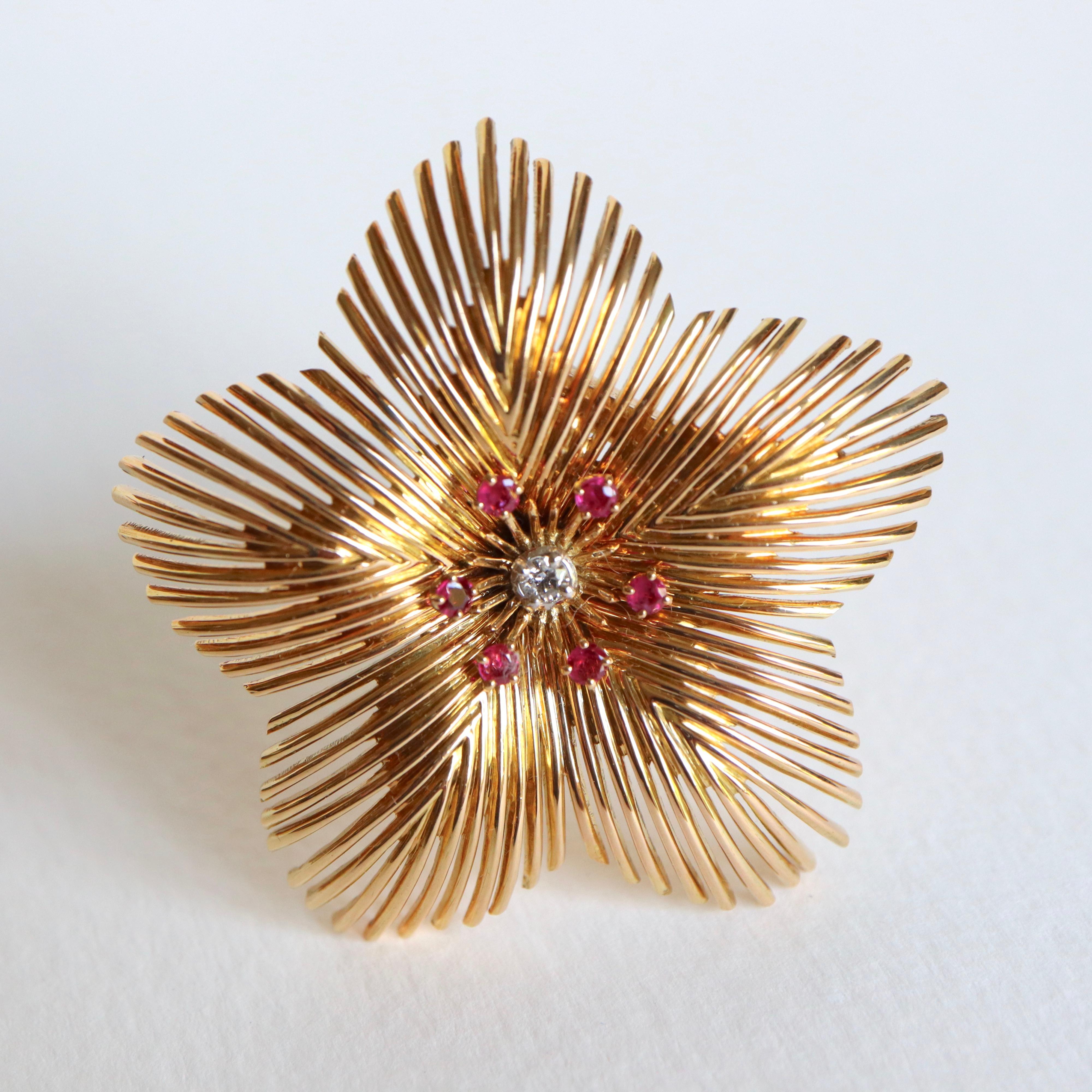Lapel clip brooch in 18 Kt yellow gold representing a 5-petalled flower adorned with 6 rubies and a central diamond.
Period 1950 
Eagle Head Hallmark. French work
Weight 18g 
Diameter: about 50mm
