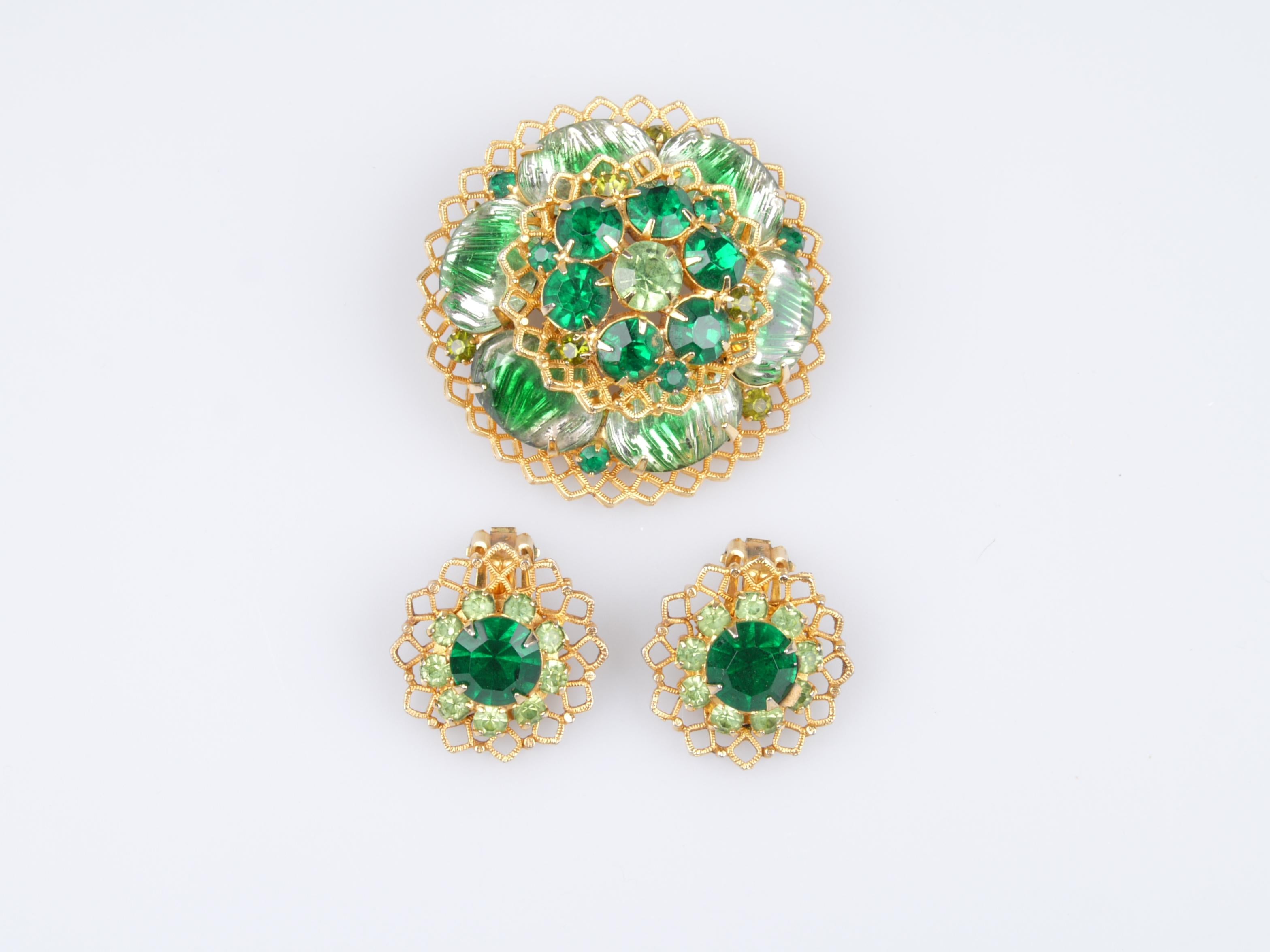 Brooch and earrings set in emerald green, 3 pieces.
Brooch and clip back earrings set with clear green stones and gold-tone filigree.
Earrings, 1 inch diameter x 0.25 inches height.
Dimensions: 2.0 inches W × 0.75 inches D.

   