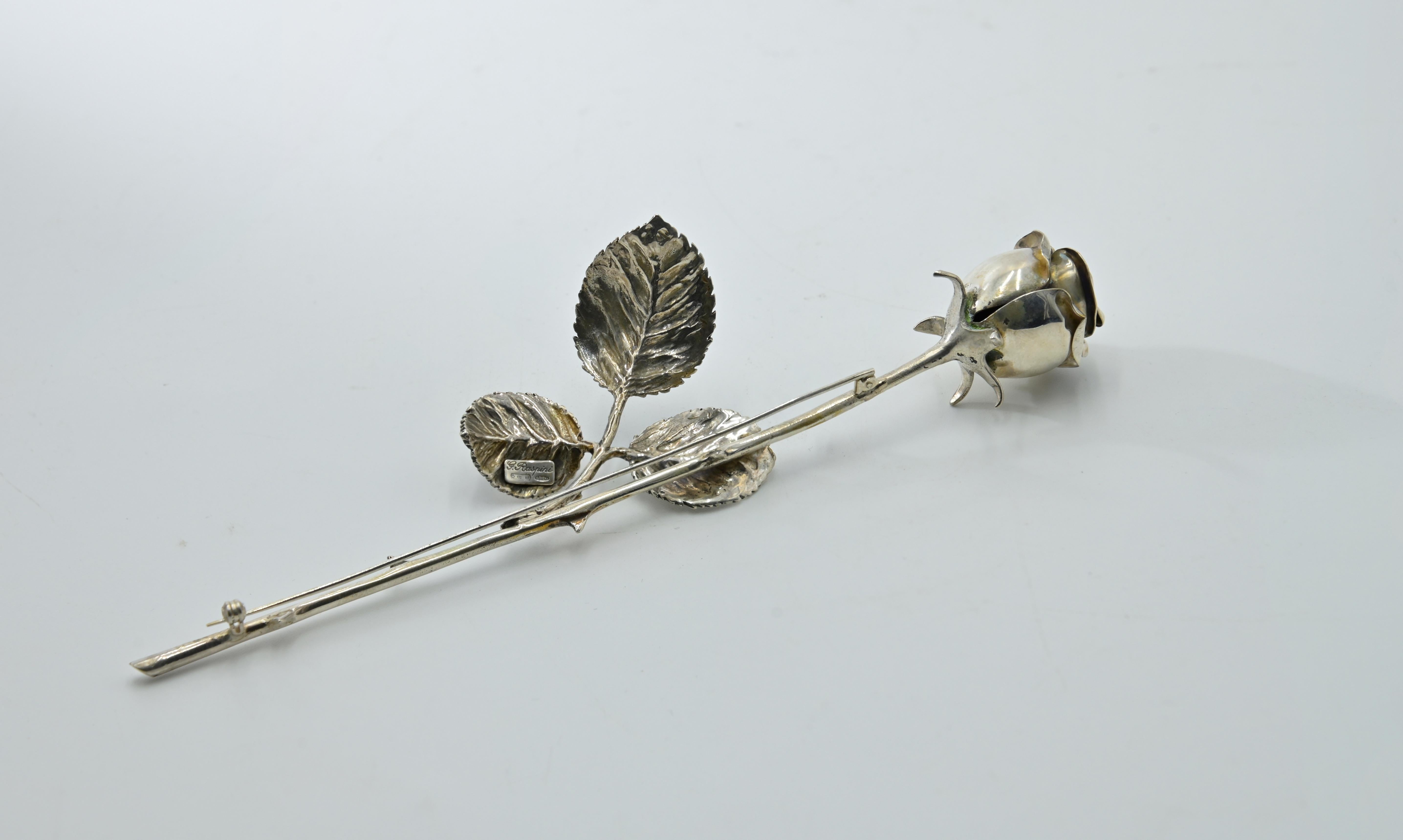 Brooch in the form of a Rose, with its original case.
Realized in Italy, Arezzo, by G. Raspini in 1960s.

Silver. L. 17.8 cm, 44 g.

Hallmarked with guarantee and maker's marks as well as with purity '800'.

Min. surface scratches. 

Good conditions 