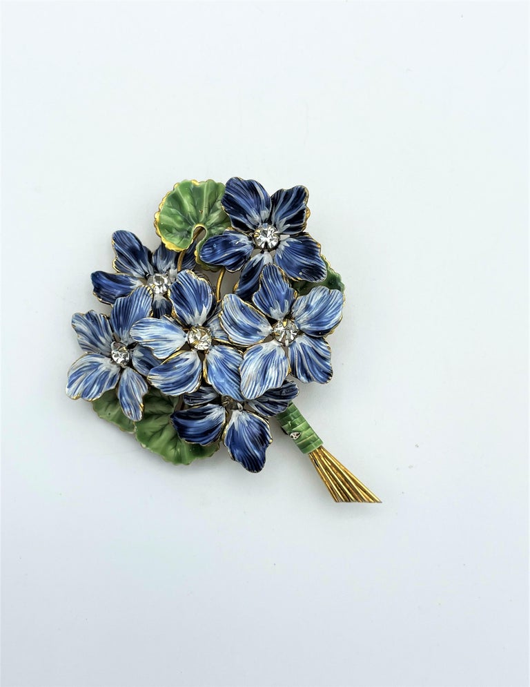 A lovely little brooch in the shape of a bunch of violets, with 6 light blue violets, in the center a small rhinestone and green leaves. It is a handcrafted enameled brooch by Sandor 1940 USA.
Measurement: Height 6 cm, flower  around  5 x 5 cm, gold