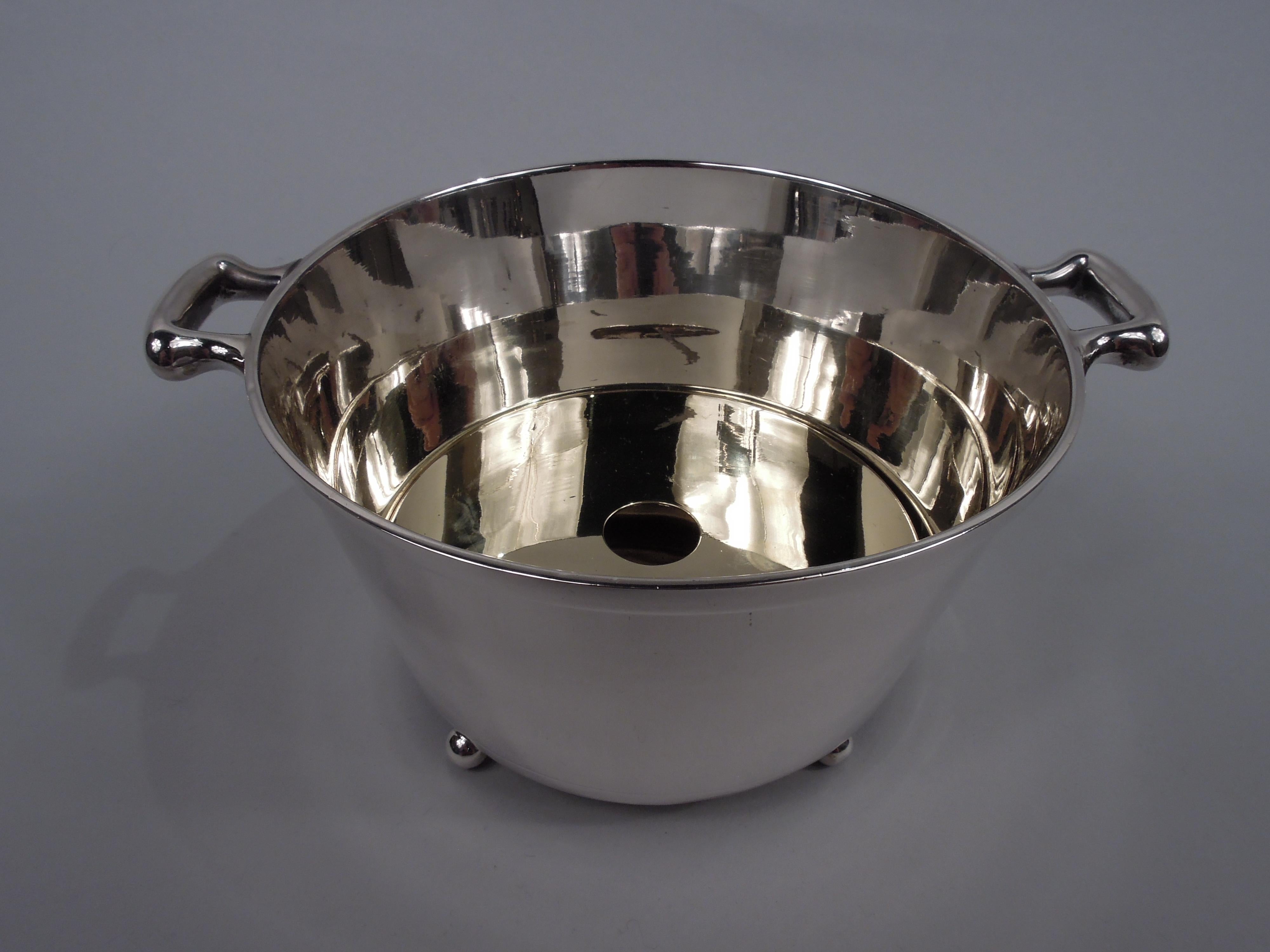 Midcentury Modern sterling silver ice bucket. Round with straight and tapering sides, overhanging rim, and engraved linear band at bottom; scroll-bracket side handles mounted to rim sides and four ball supports. Detachable gilt brass liner. Fully