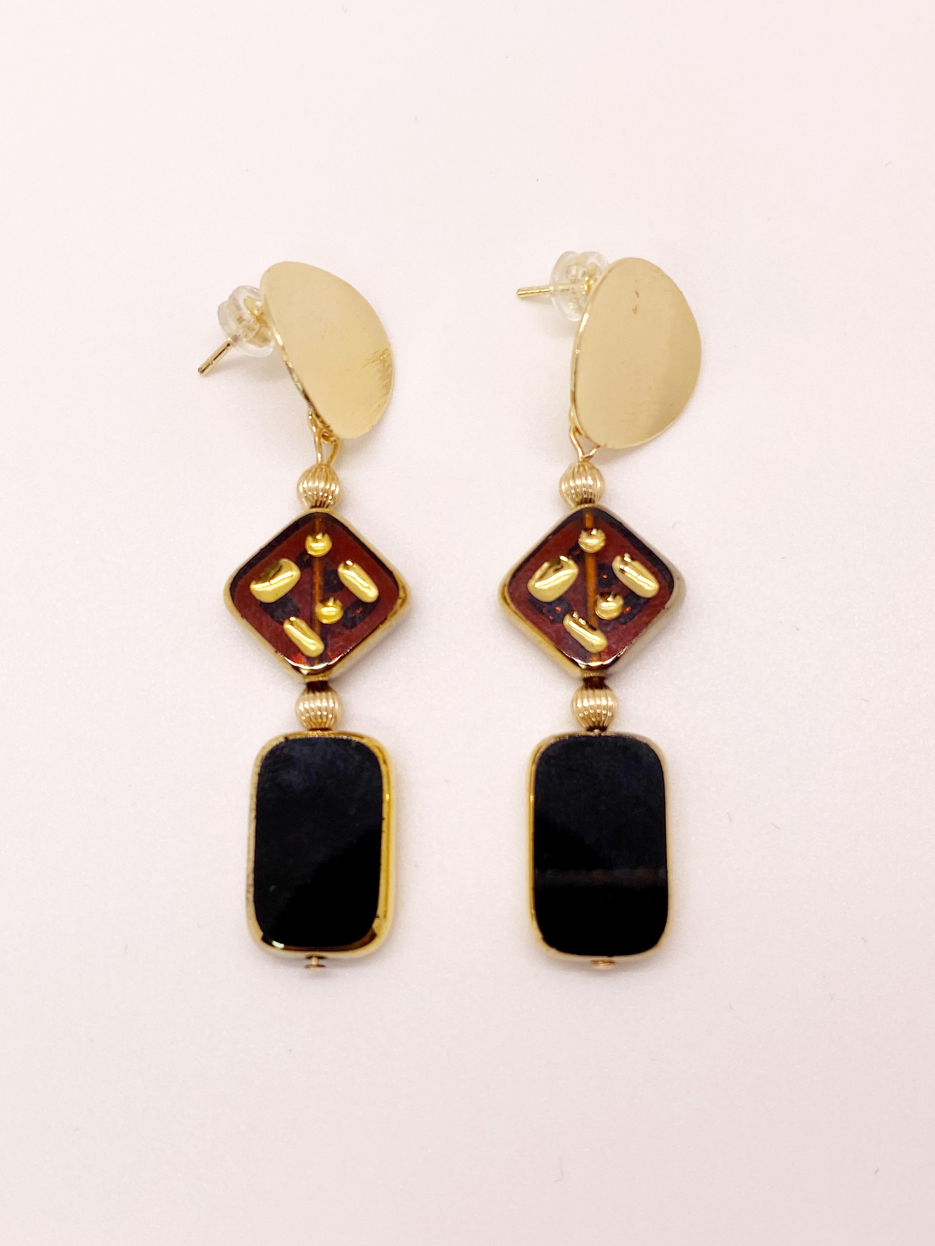 These earrings are composed of a translucent brown amber glass beads with etched design and a black tile bead. These are vintage German glass beads that have been edged with 24K gold. They dangle on 14K gold-filled ear finding post. 

The German