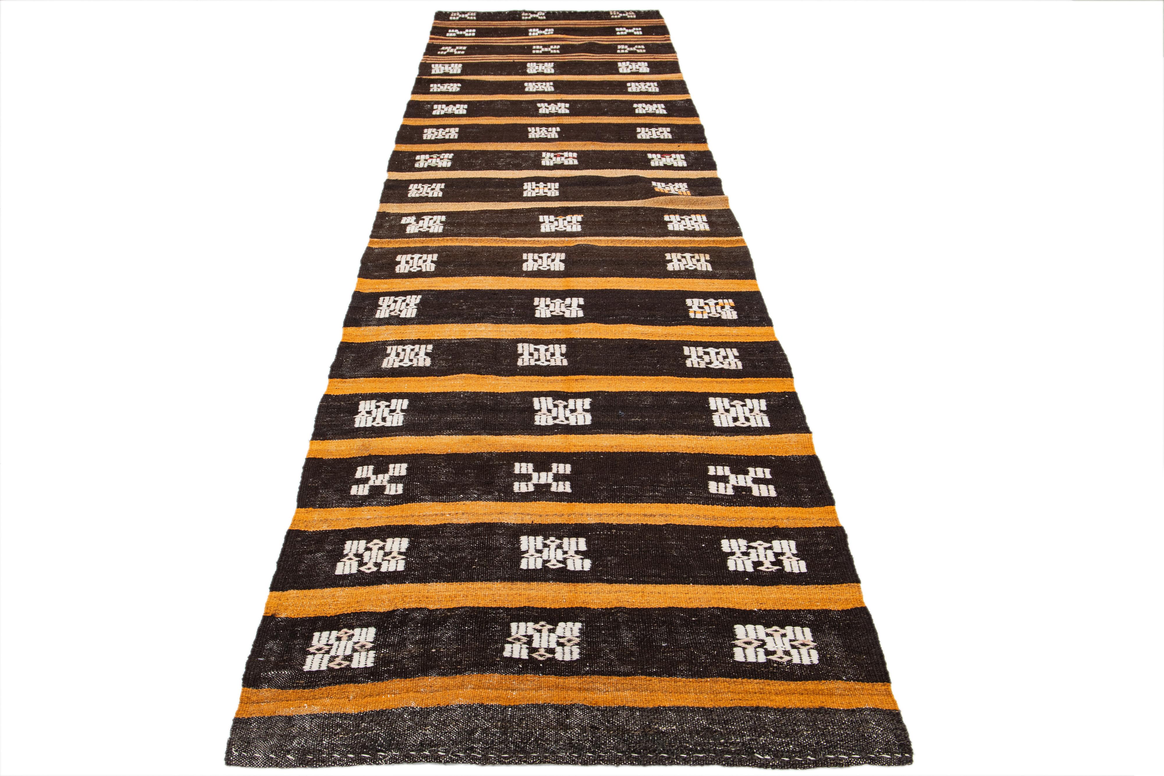 Handmade wool kilim rug with a brown color field and orange striped accent. Features an all-over ivory design.

This rug measures 3'6
